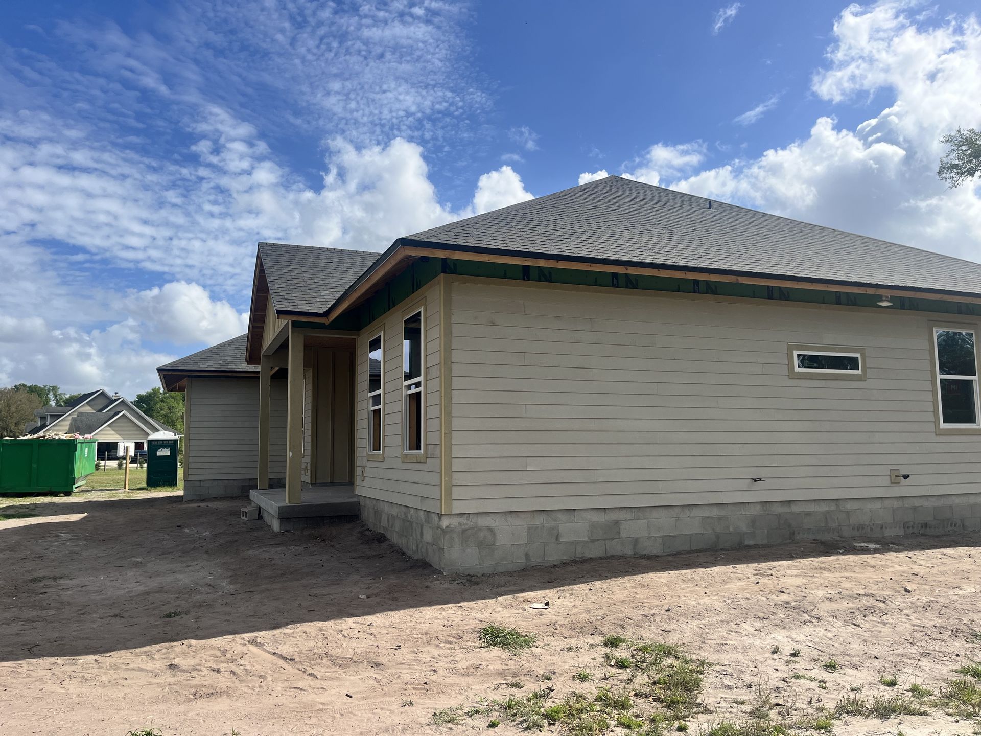 New beige house exterior with a gray roof and cloudy blue sky overhead
