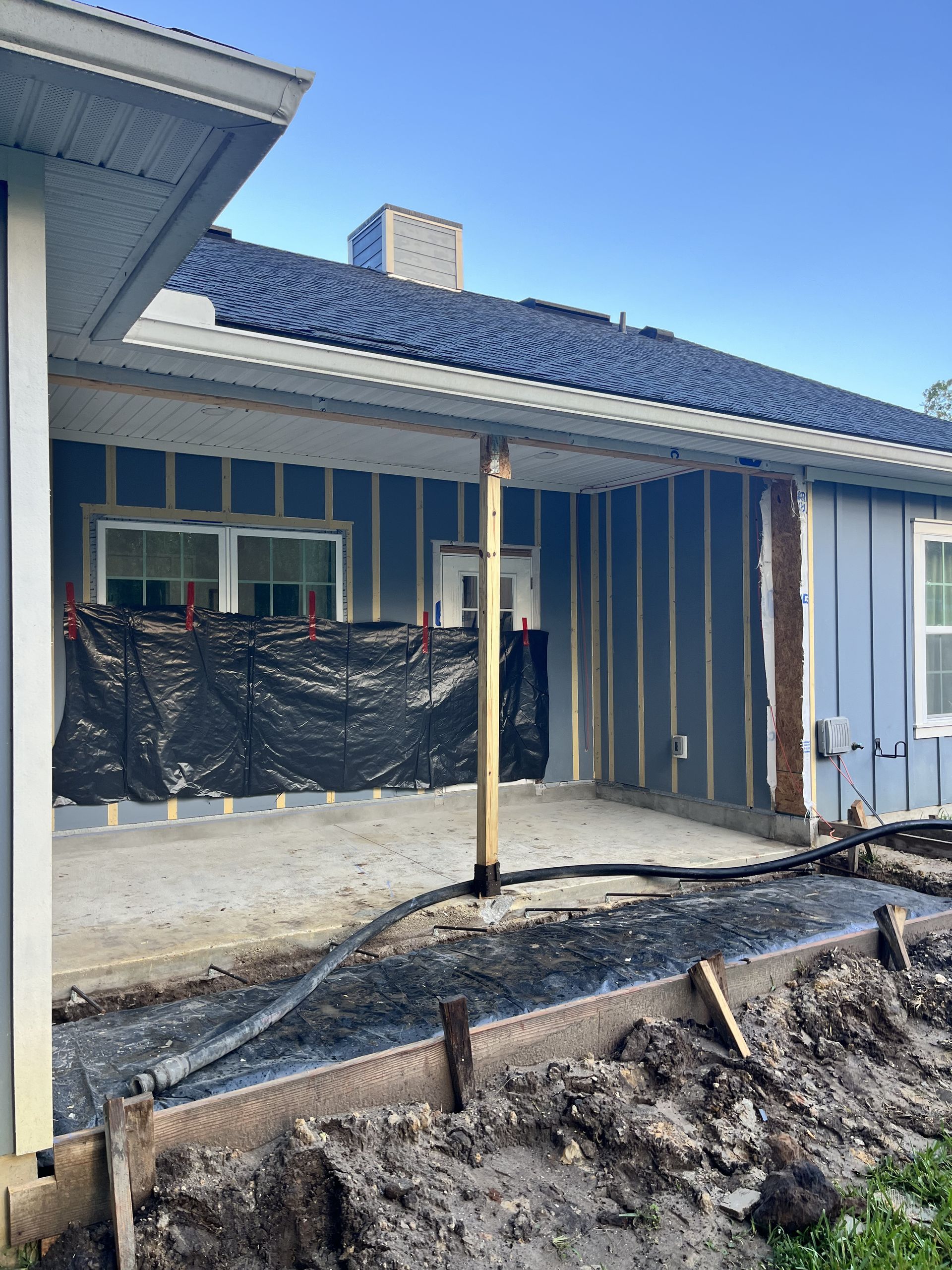 Blue house exterior under construction with exposed dirt yard and covered windows