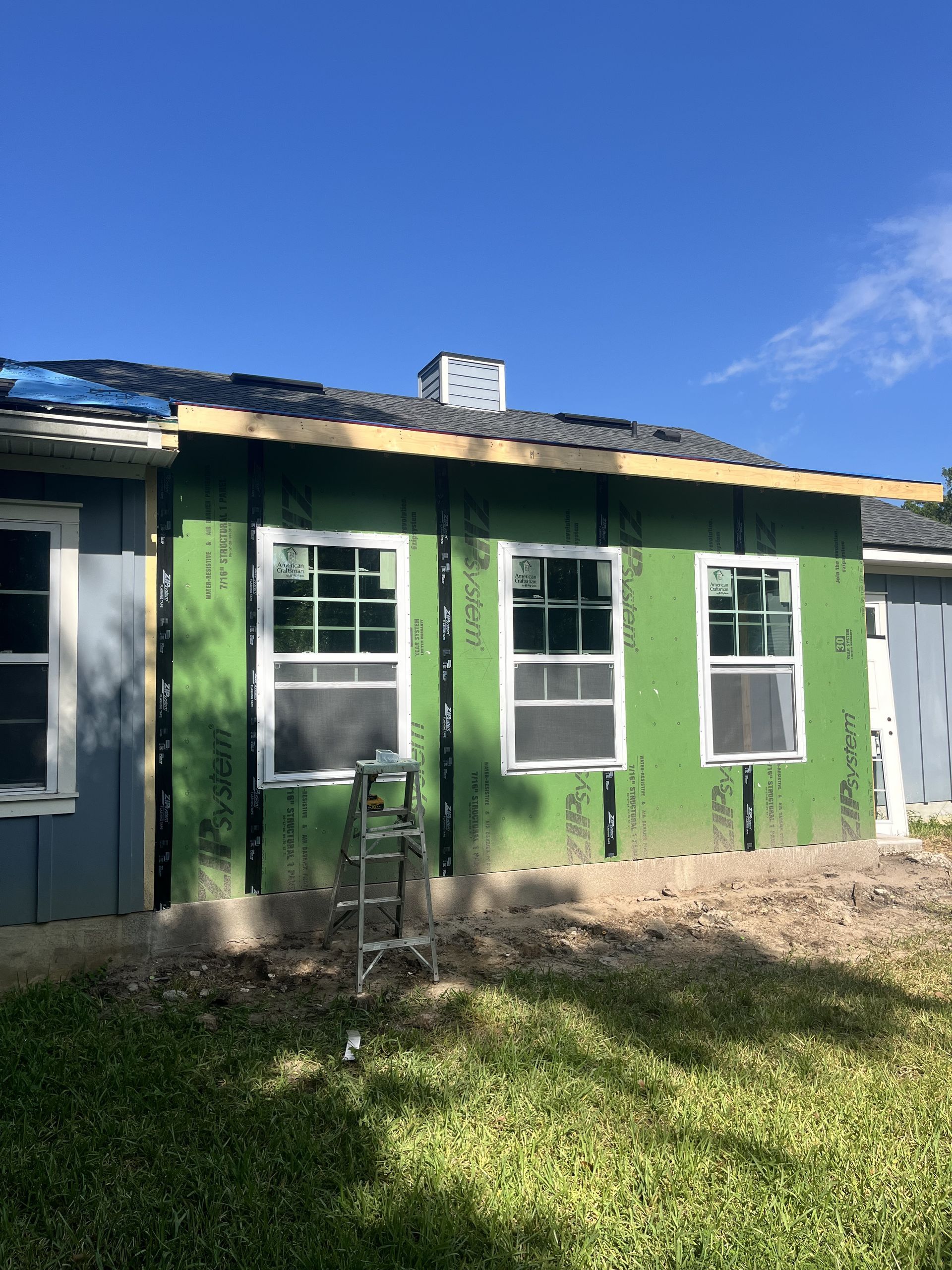 Green house exterior with white-trimmed windows and a blue roof under a clear sky