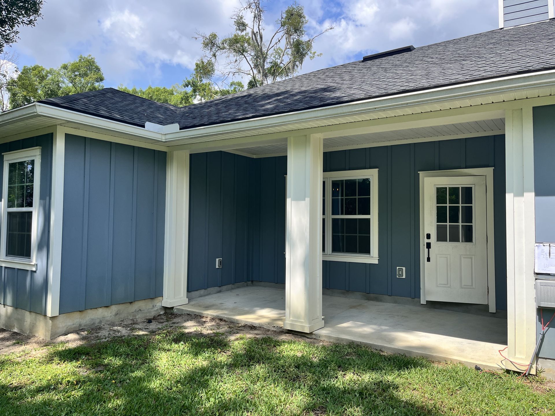 Blue house exterior with white trim, covered porch, and grassy yard under a partly cloudy sky