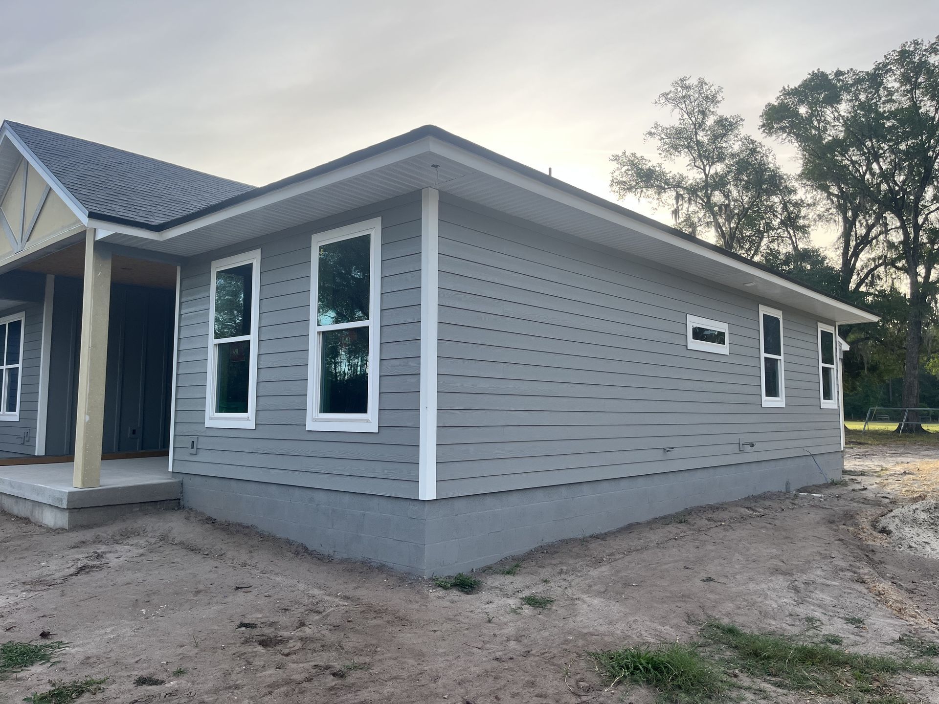 New gray house exterior with white trim, front porch, and unfinished dirt yard