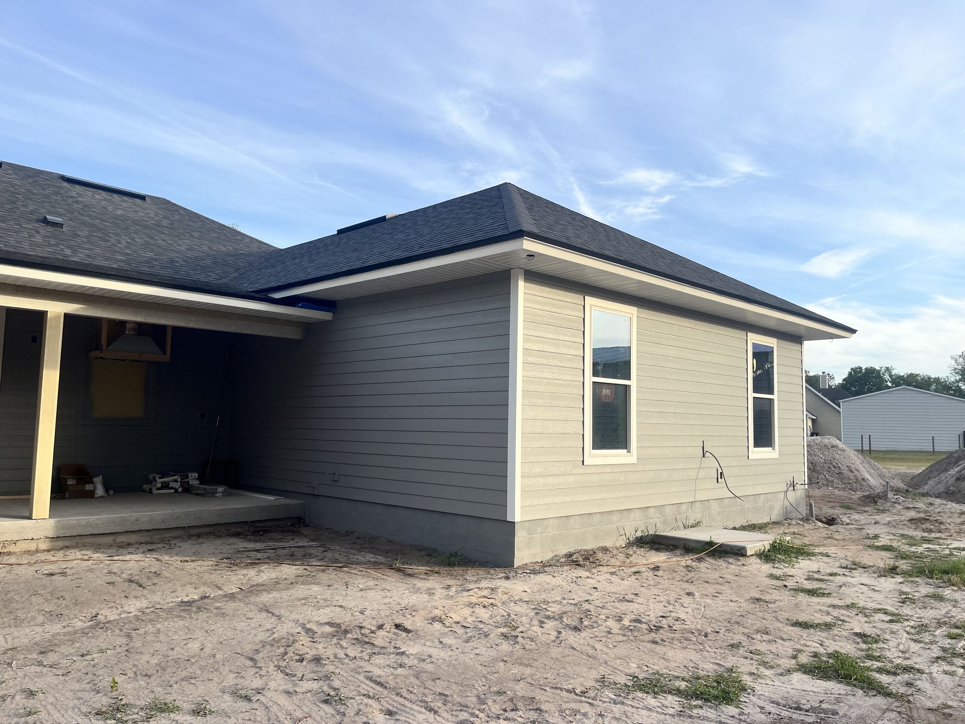 New beige house exterior with dark roof, side wall, and dirt yard under construction