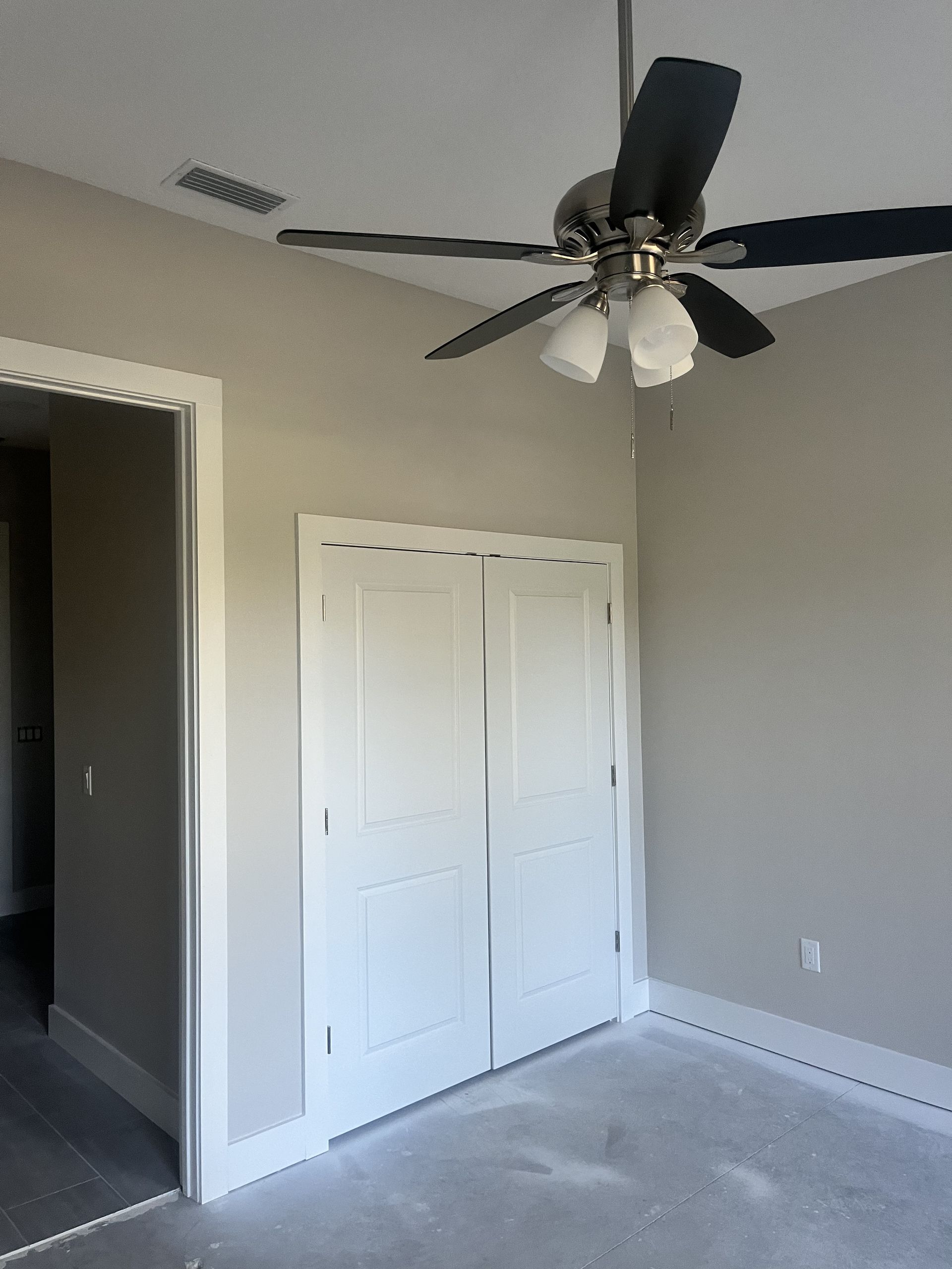 Empty beige bedroom with a ceiling fan, white closet doors, and gray carpet.