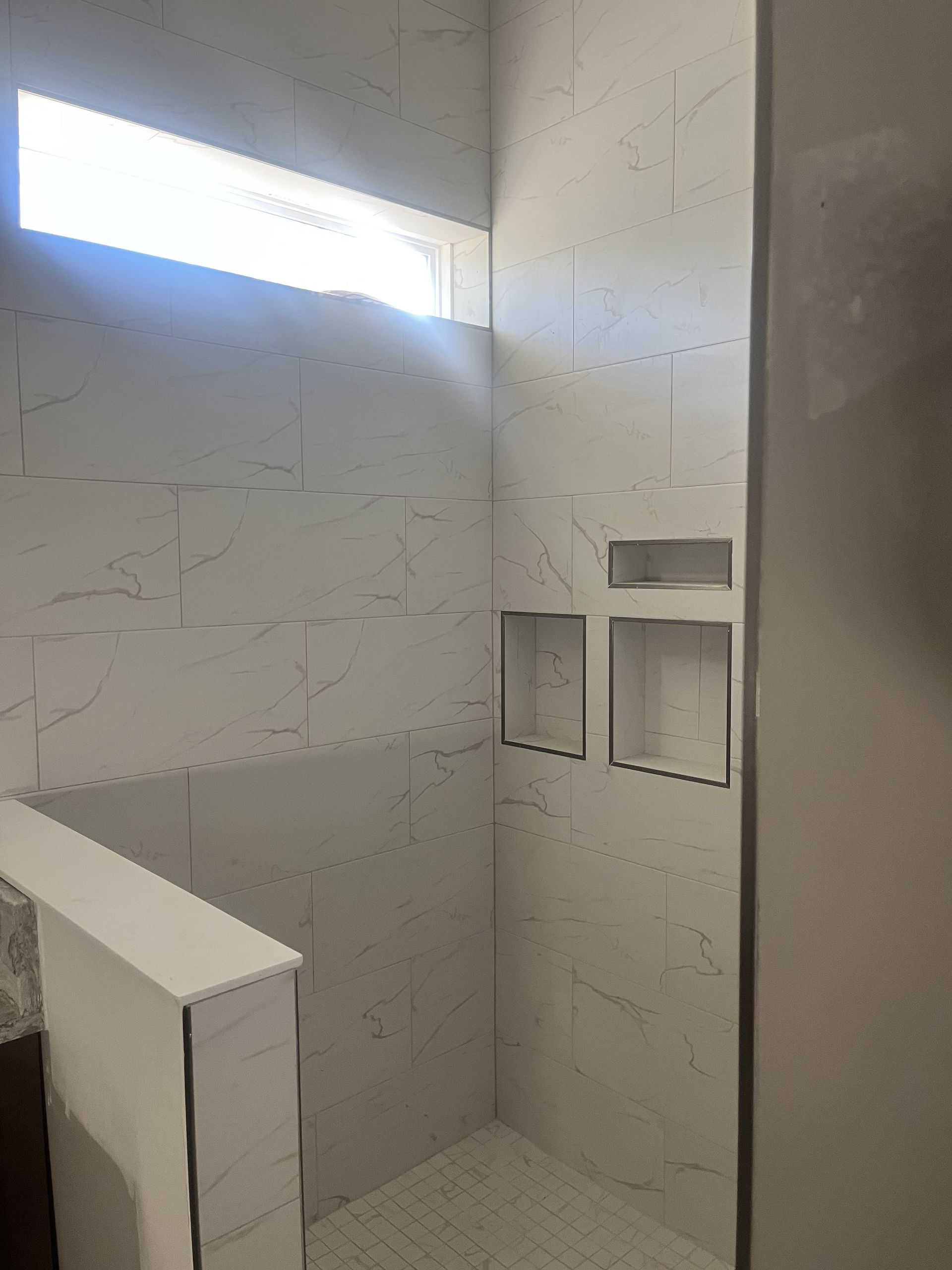 White tiled shower stall with a small high window and built-in wall niches