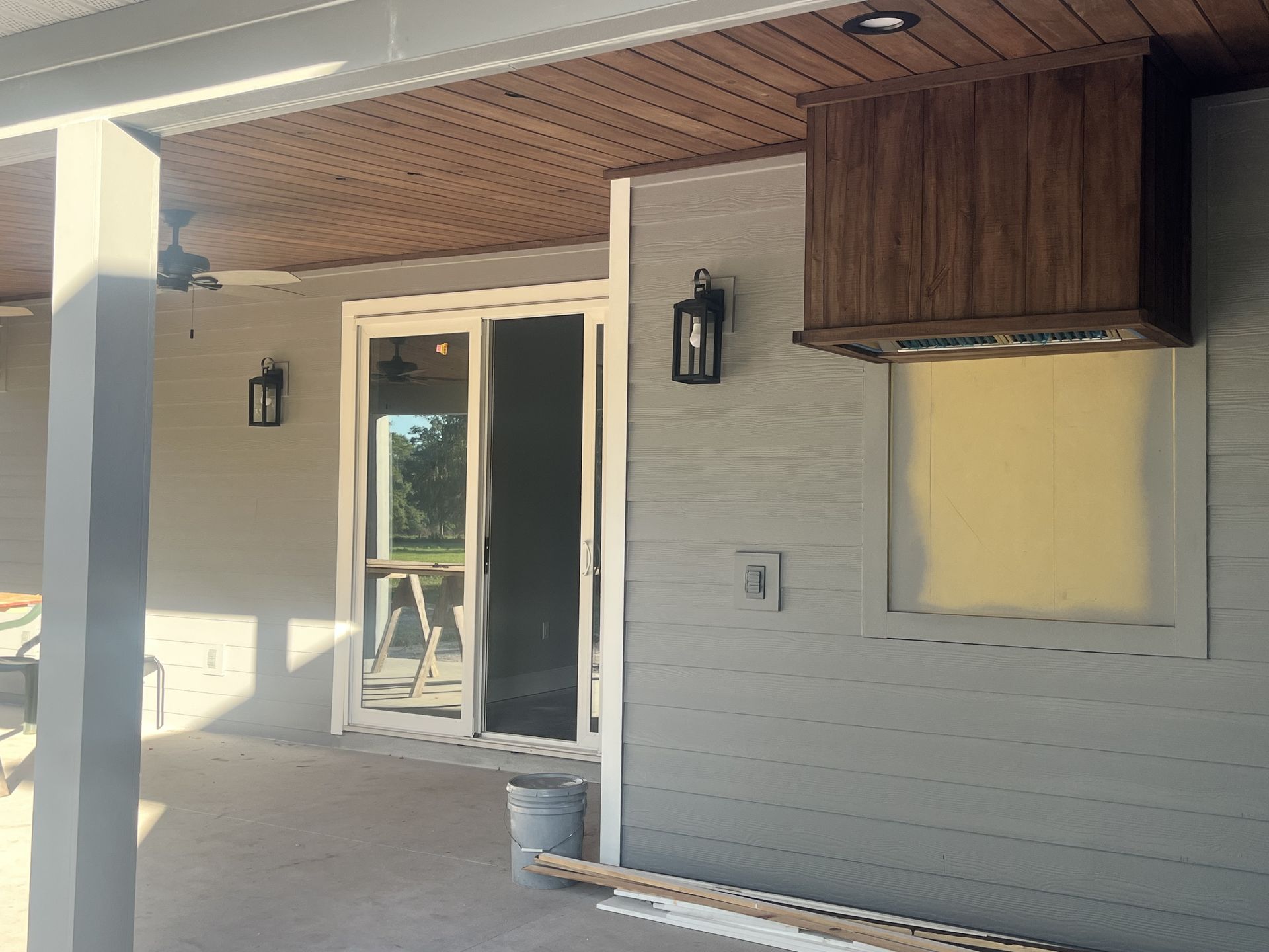 Covered patio with white brick wall, sliding glass door, wall sconces, and wood-accented ceiling