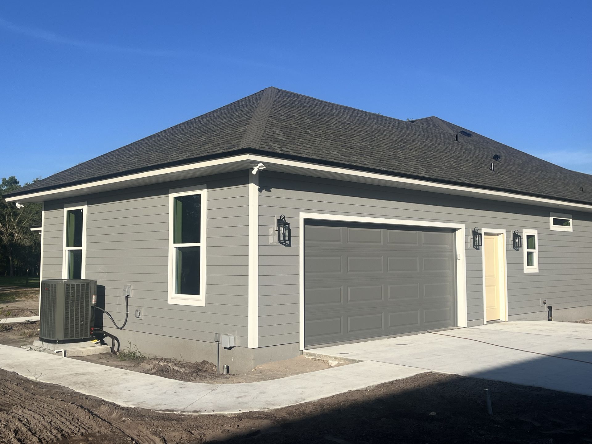 Gray house with dark roof, attached garage, and small concrete patio under a clear blue sky