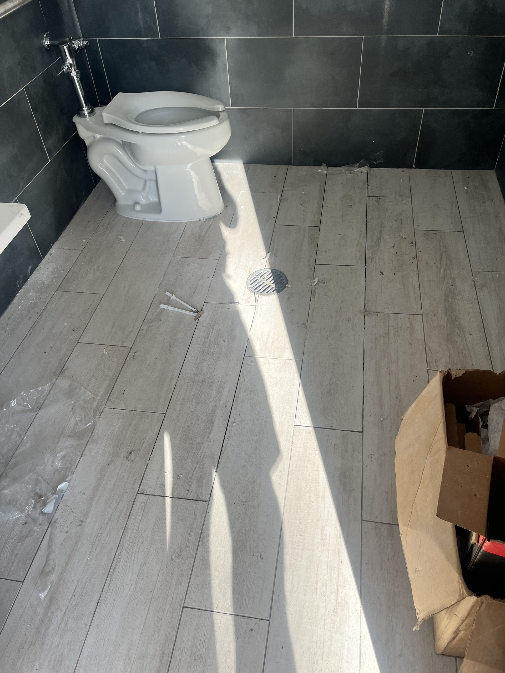 Small tiled bathroom with a toilet and an open cardboard box on the floor, lit by a bright shaft of sunlight.