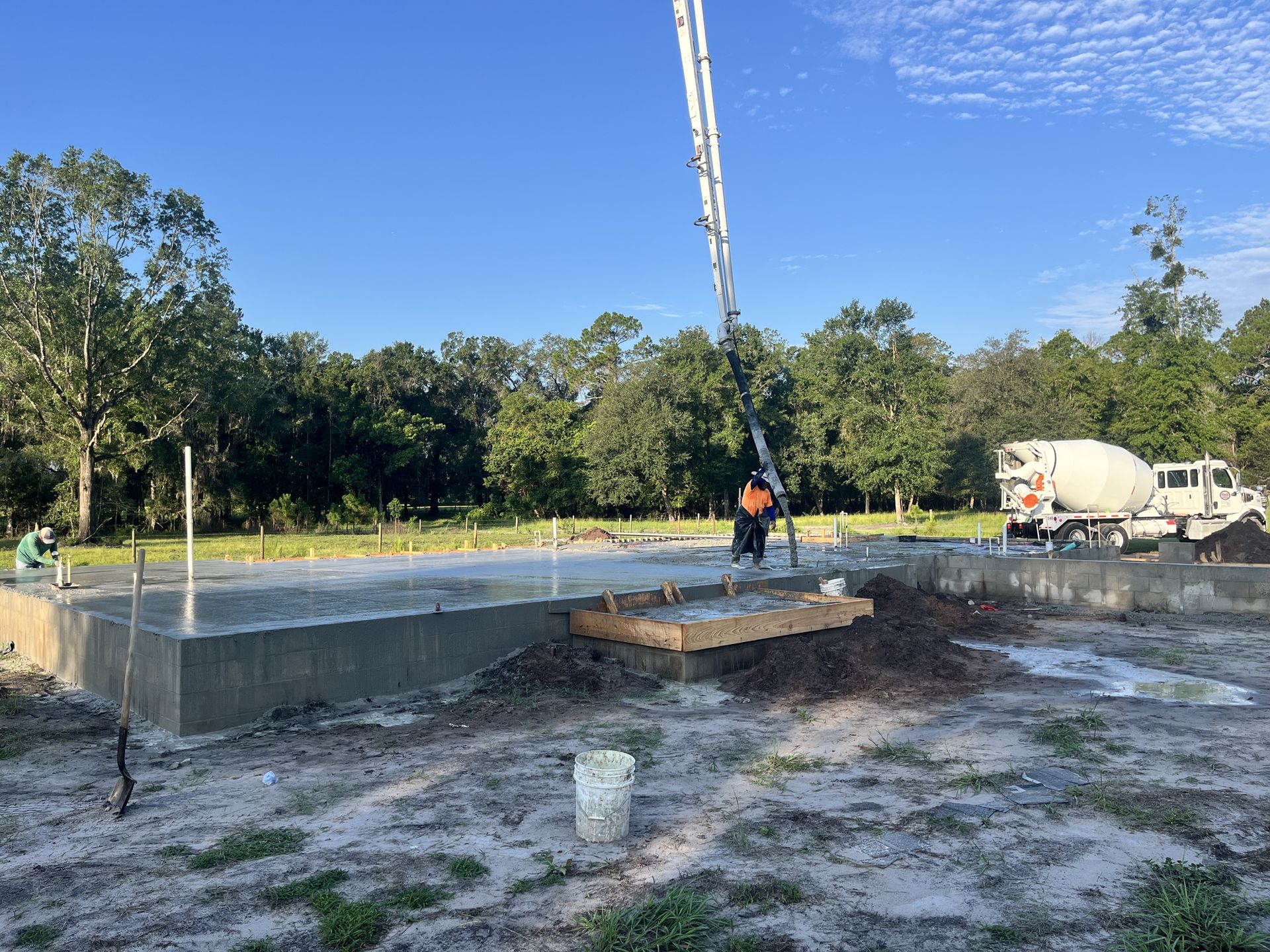 Construction site with concrete slab, worker near forms, and cement truck under a blue sky