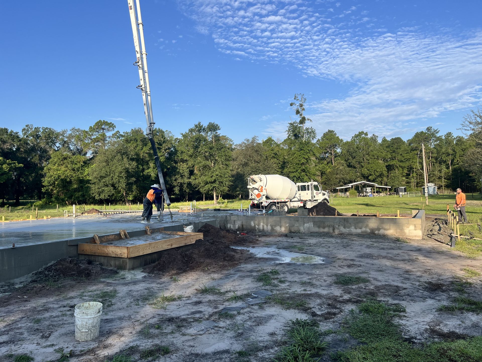 Construction site with concrete foundation, workers, and cement truck under a blue sky