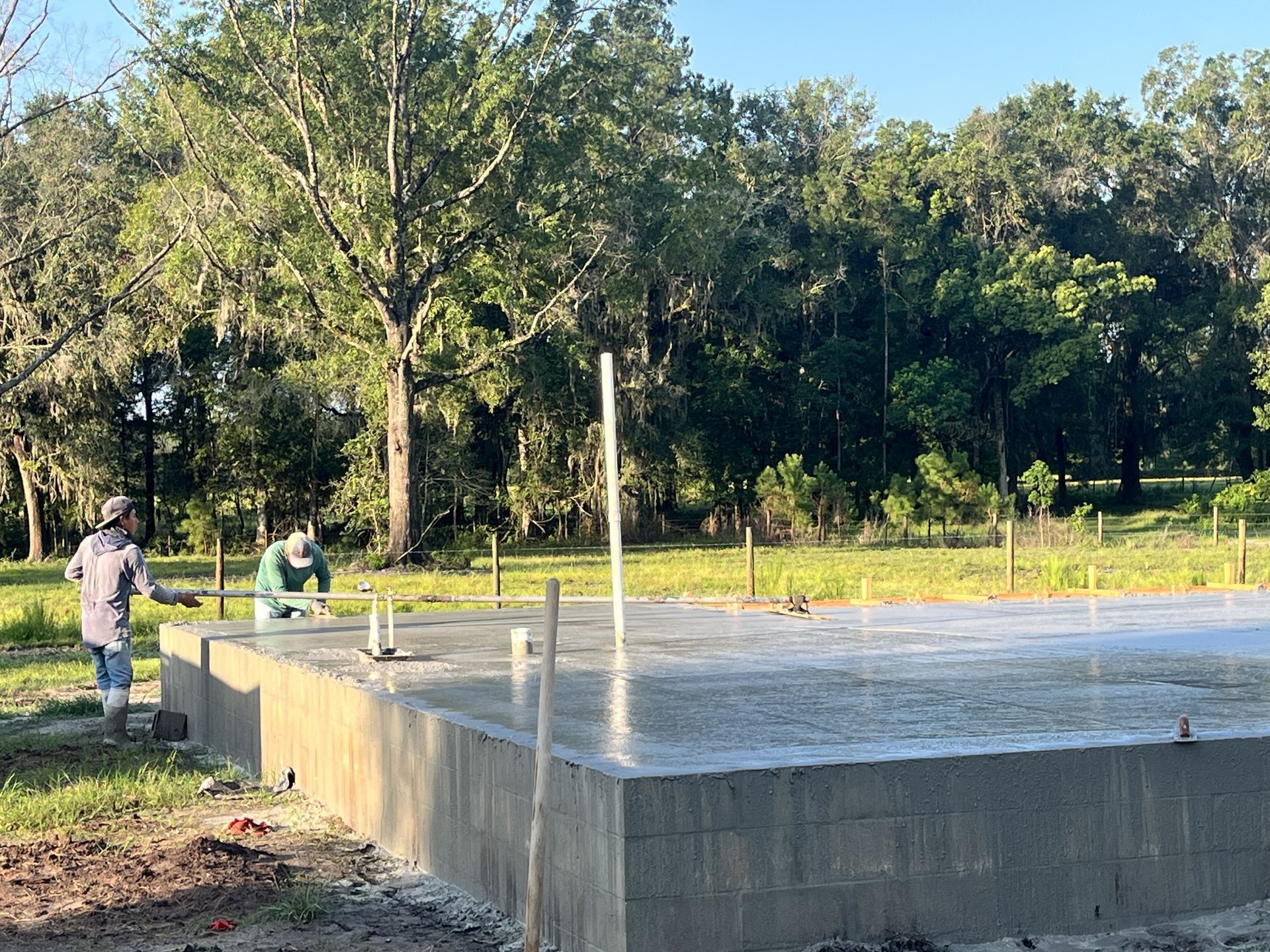 People standing beside a raised concrete foundation at a wooded construction site.