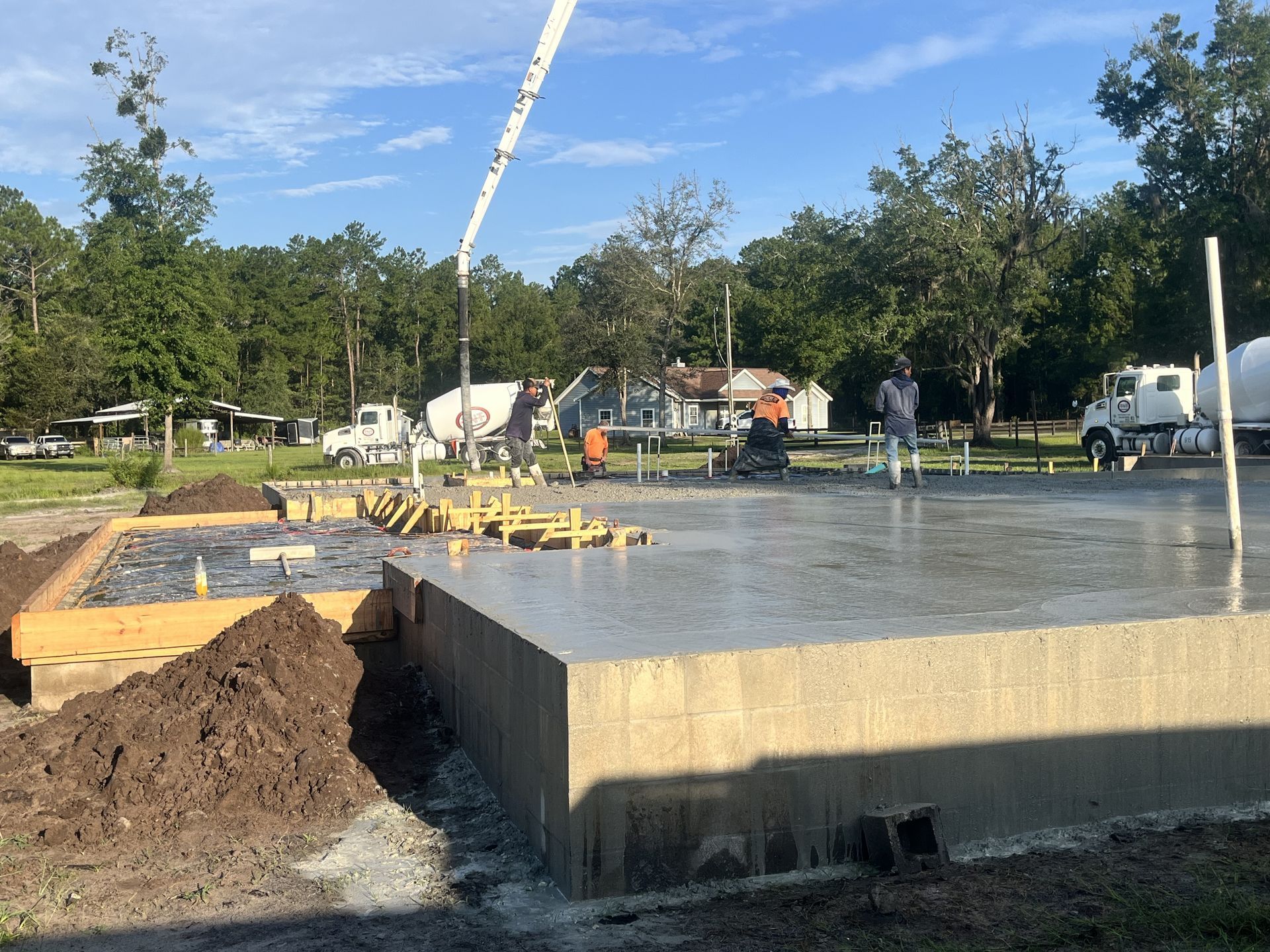 Concrete foundation being poured at a construction site, with workers and a pump truck nearby.
