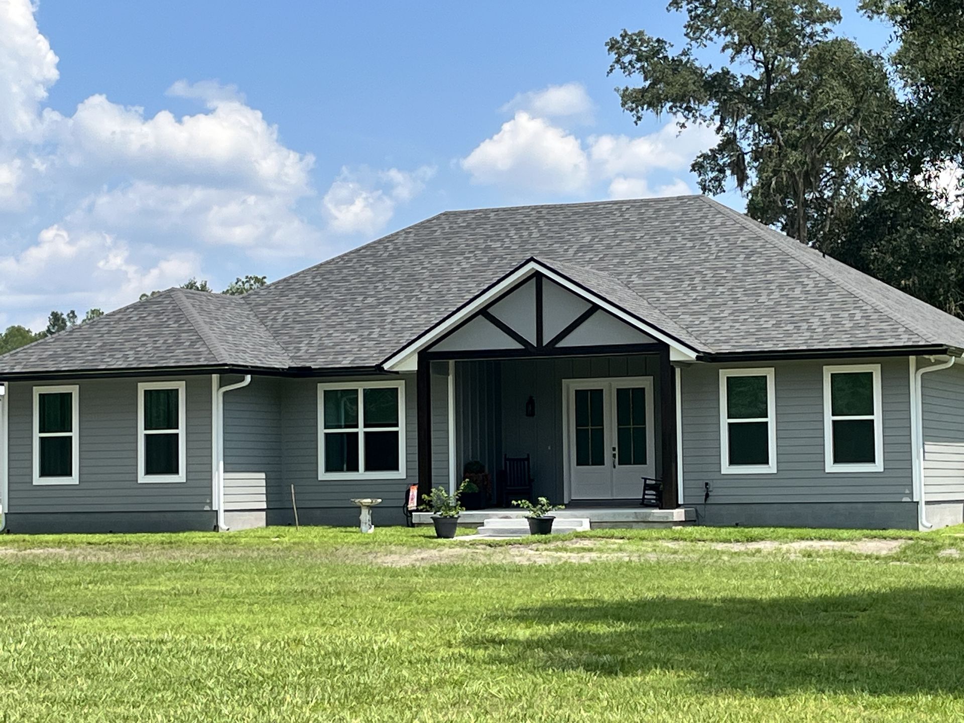 Single-story gray house with a front porch, white trim, and a large green lawn under a blue sky