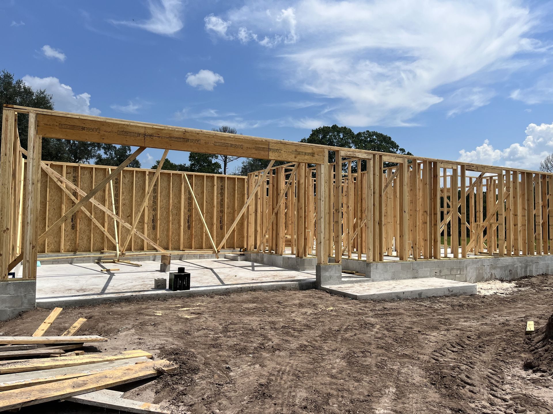 Partially built wooden house framing on a concrete foundation under a blue sky