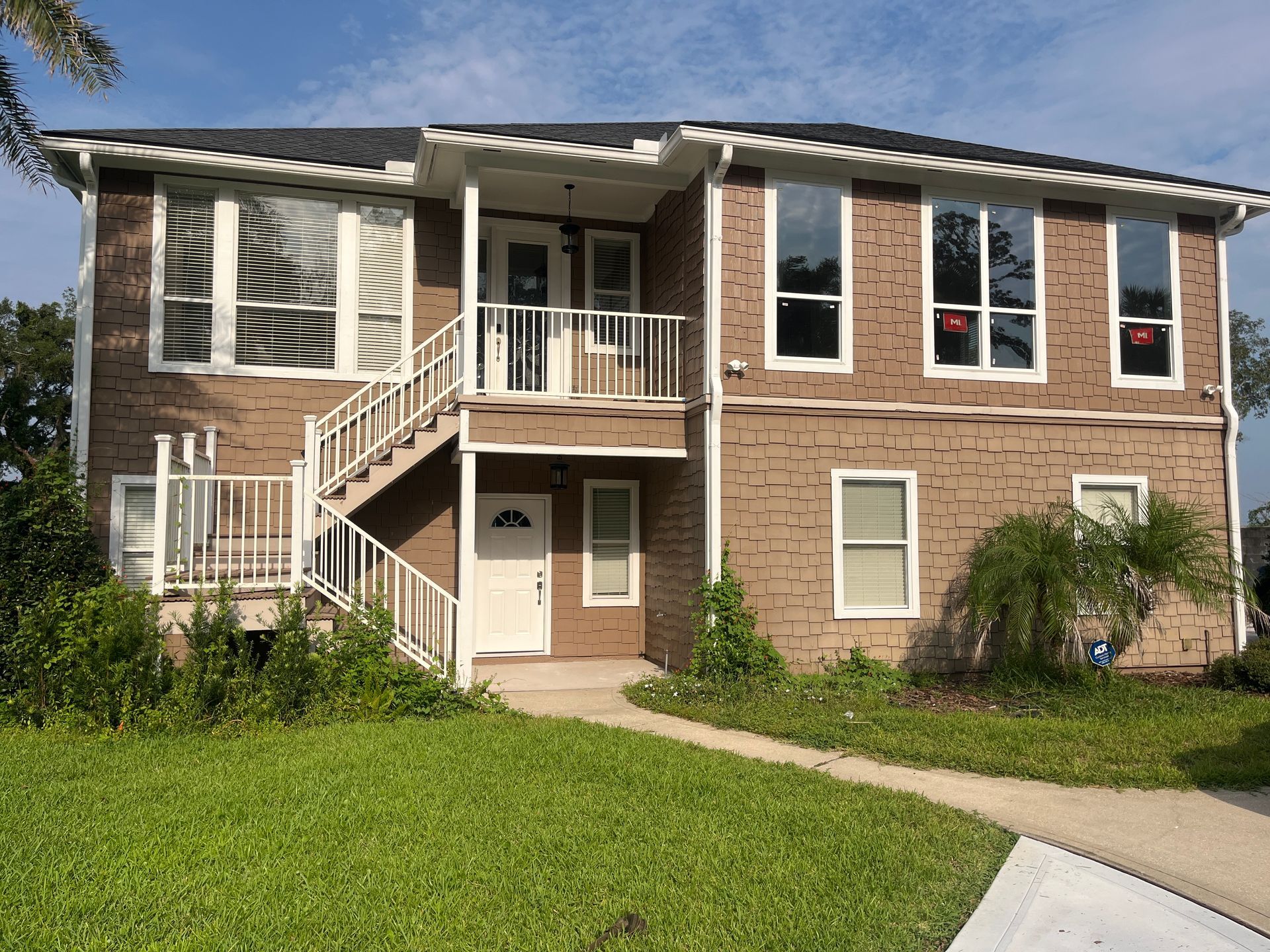 Two-story brick apartment building with white trim, balconies, stairs, and a grassy lawn in front