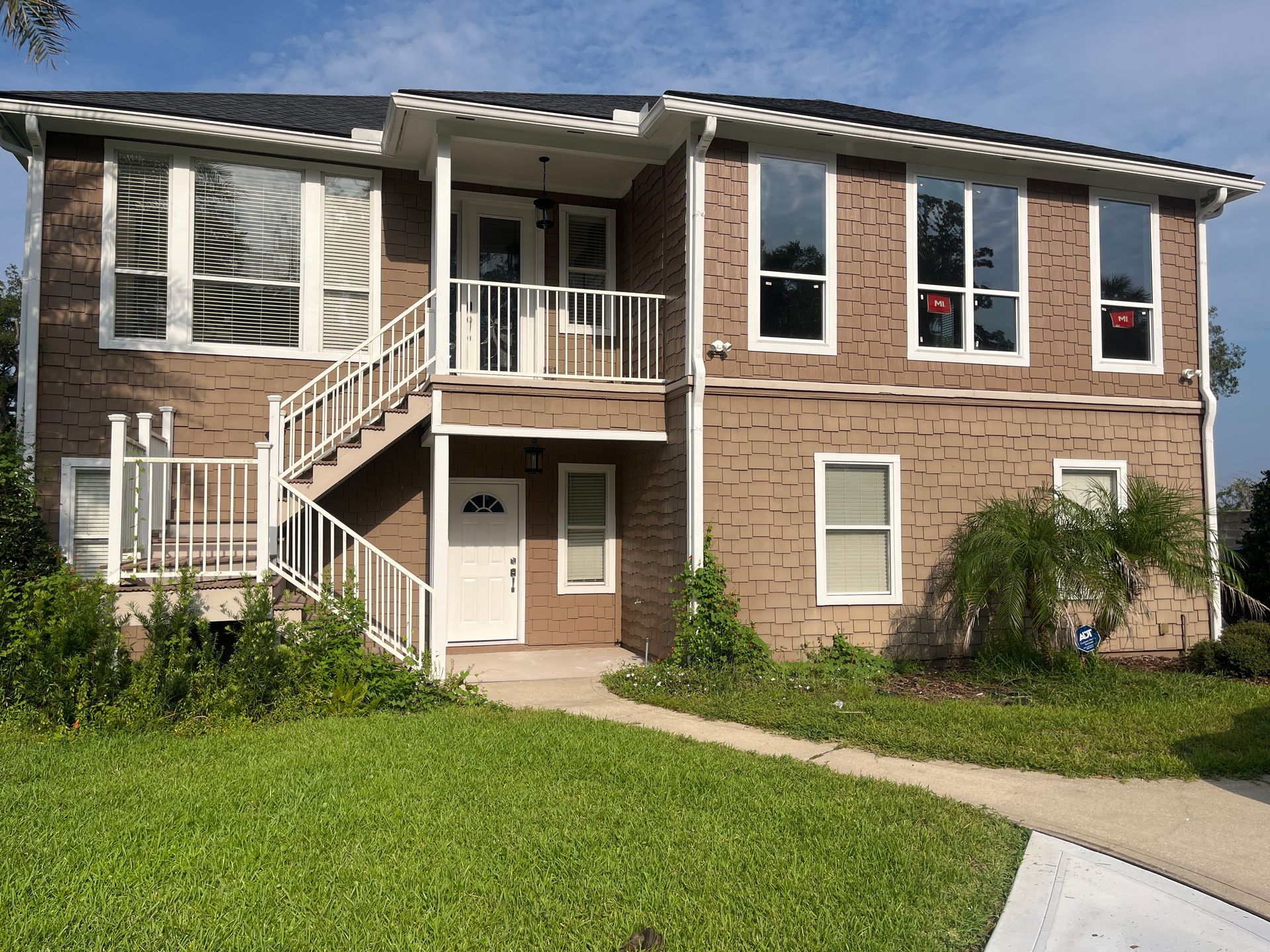 Two-story brick apartment building with white staircases, balconies, and a green lawn in front