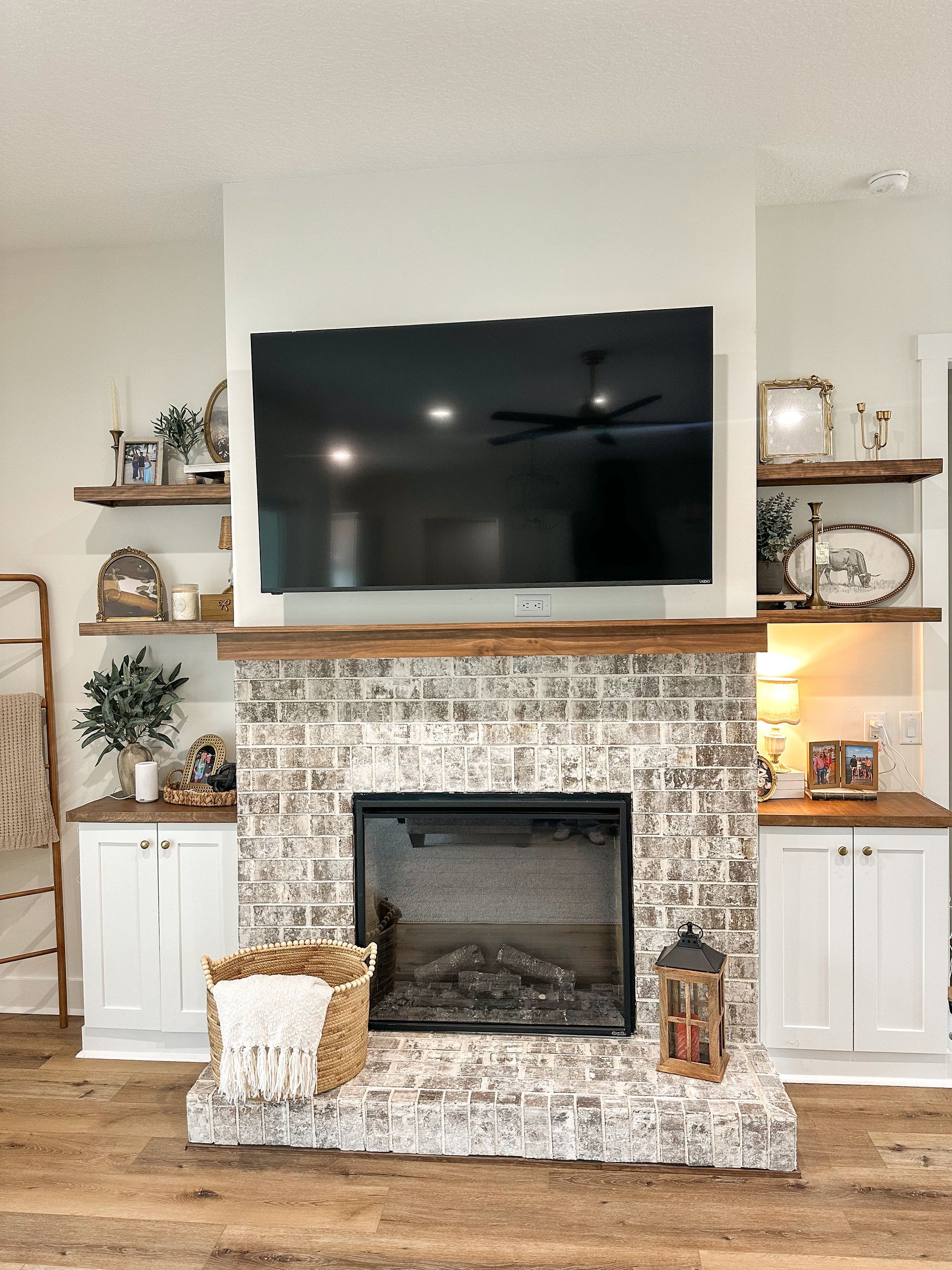 Living room fireplace with large wall-mounted TV, rustic mantel, and white cabinets and shelves on both sides