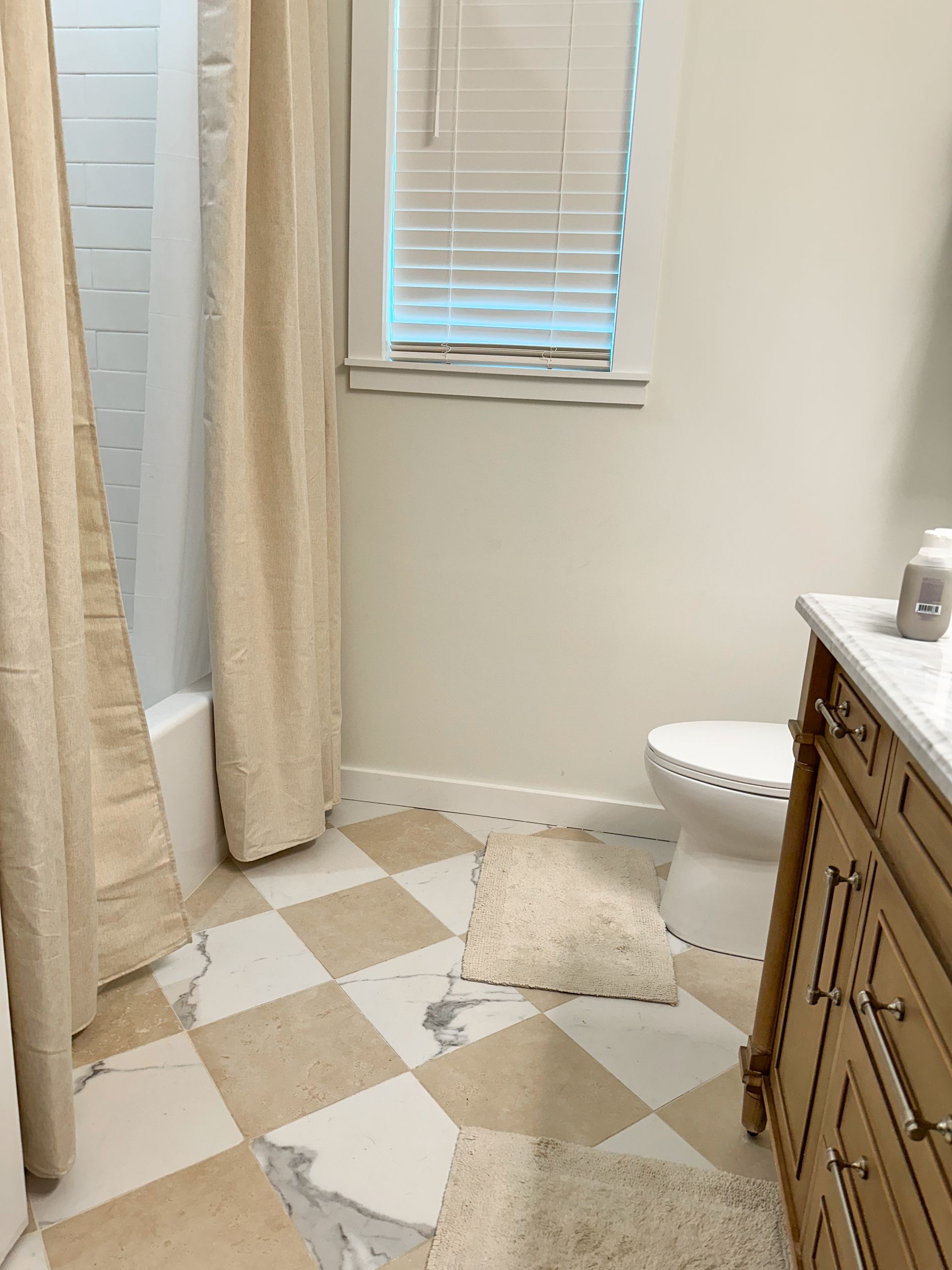 Small bathroom with checkered tile floor, shower curtain, window, toilet, and wood vanity; water on floor near toilet.