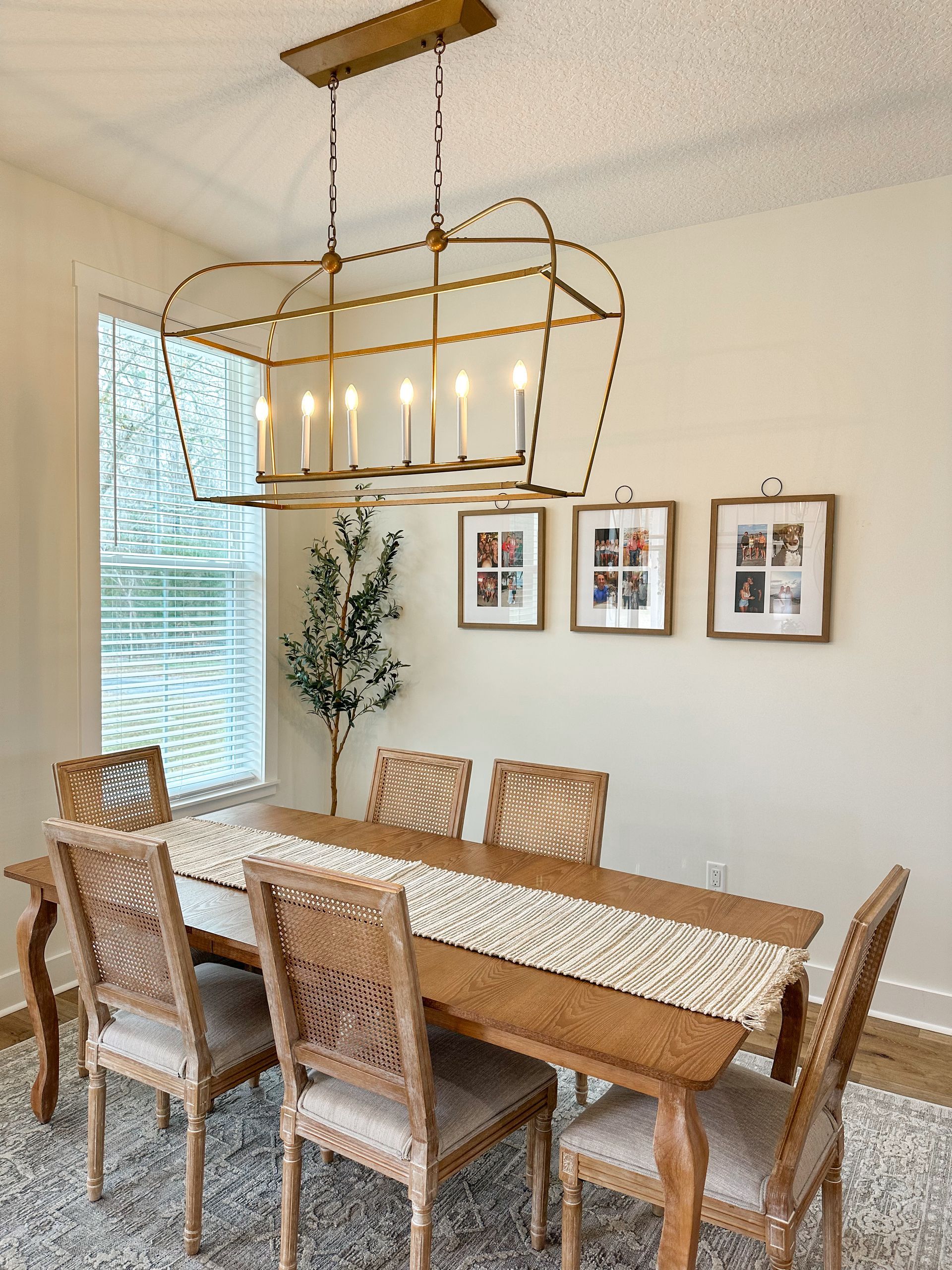 Dining room with wooden table, six chairs, brass chandelier, wall art, and window blinds