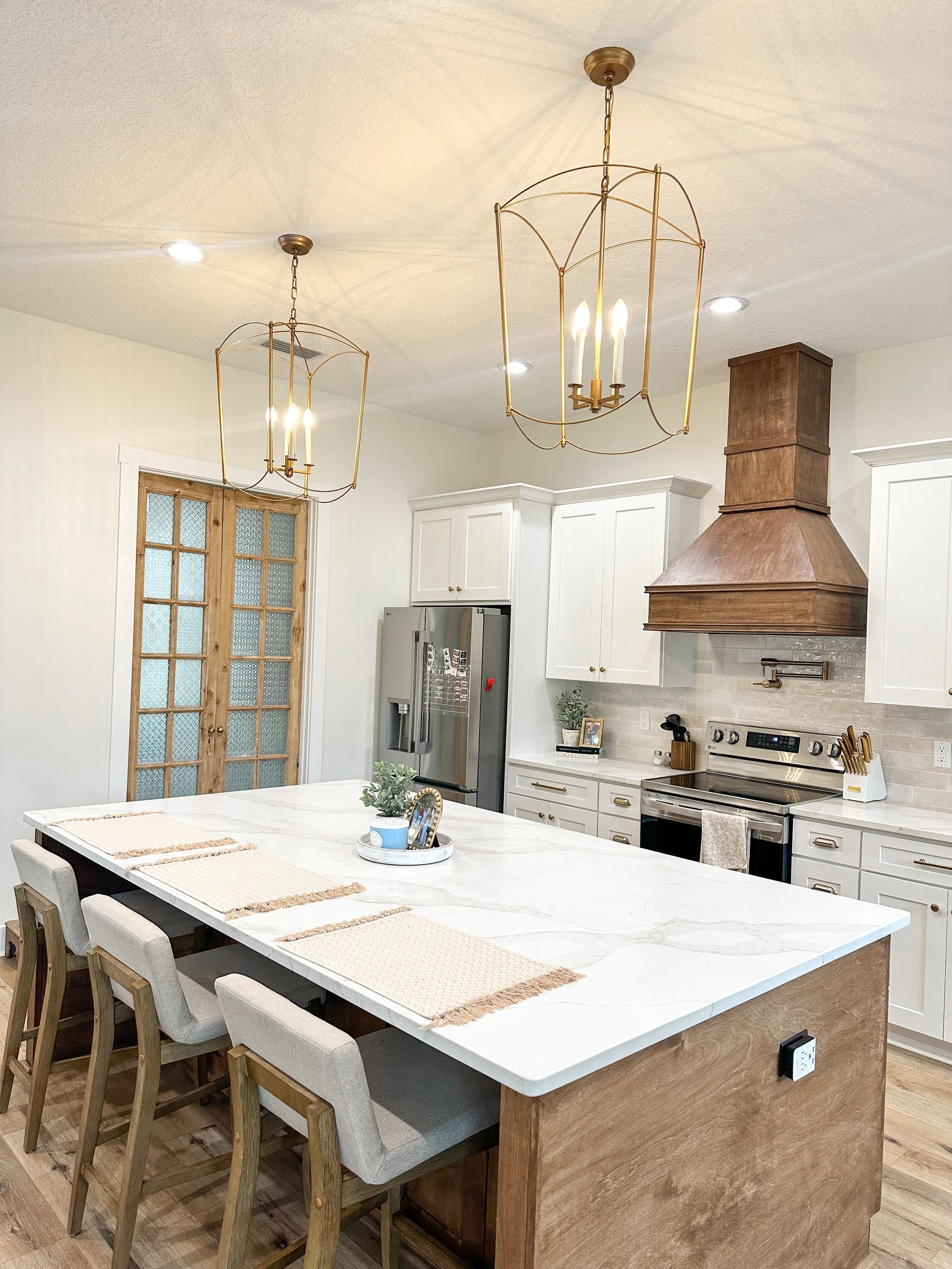 Modern kitchen with white island, wood accents, pendant lights, stainless fridge, and copper range hood