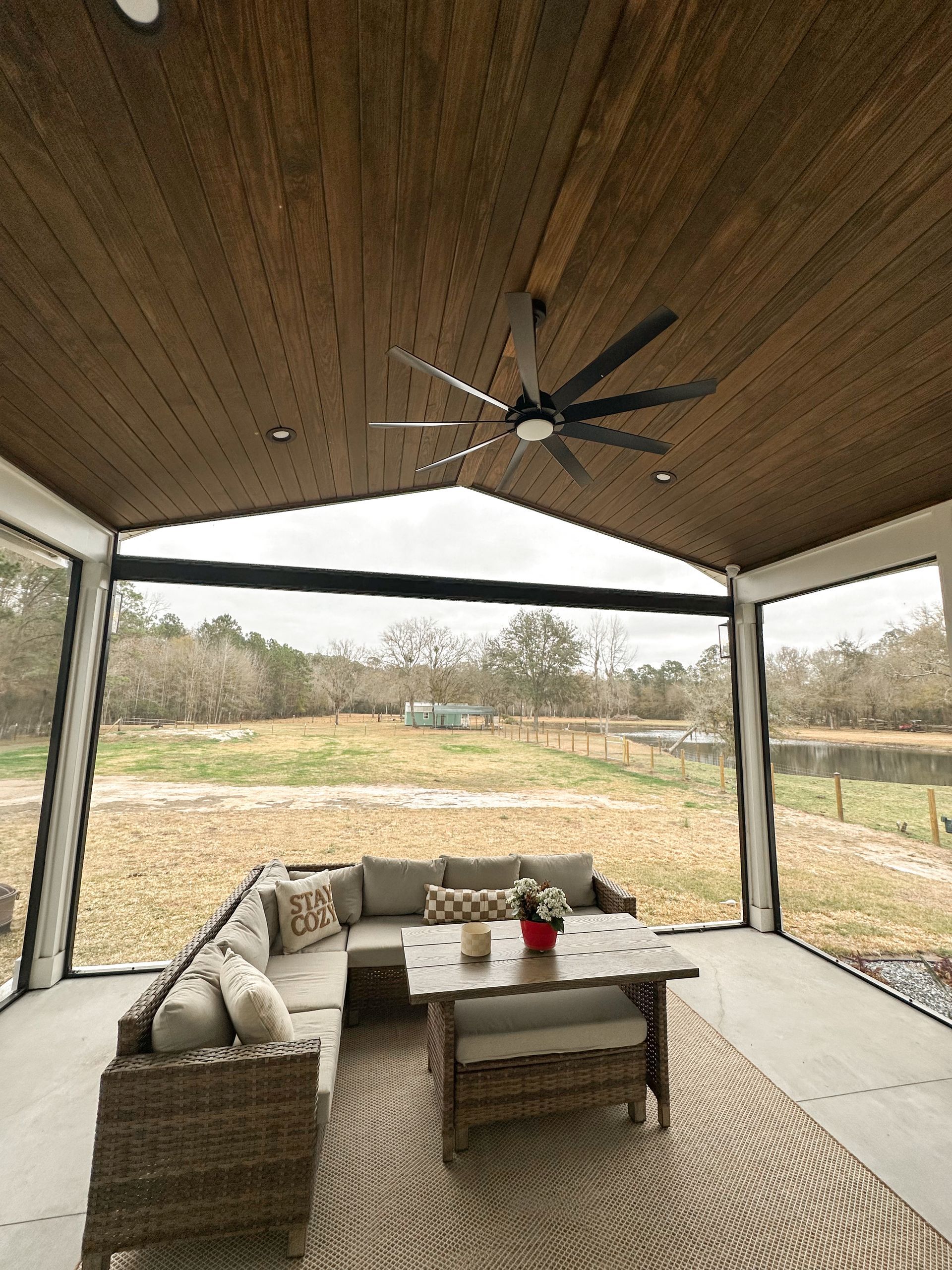 Covered patio with wicker sectional, coffee table, ceiling fan, and open view of a grassy yard