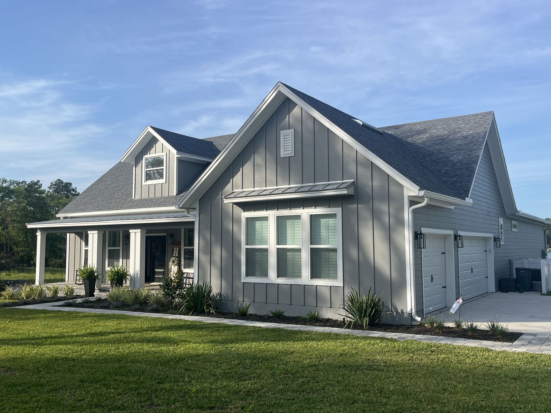 Gray suburban house with white trim, front porch, and manicured lawn under a blue sky
