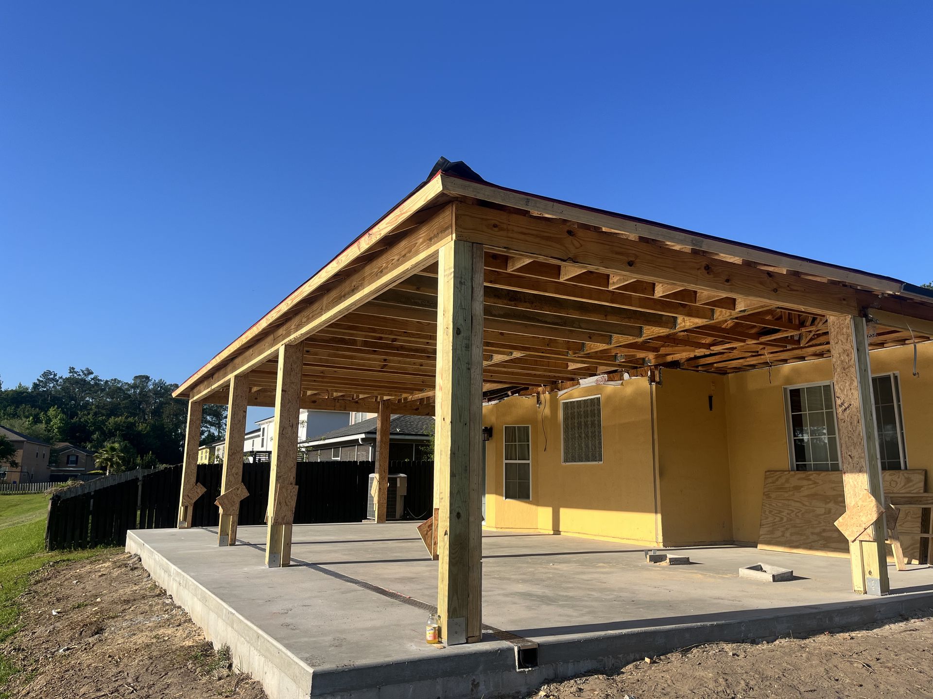 Unfinished wooden house with a covered porch and concrete slab under a bright blue sky