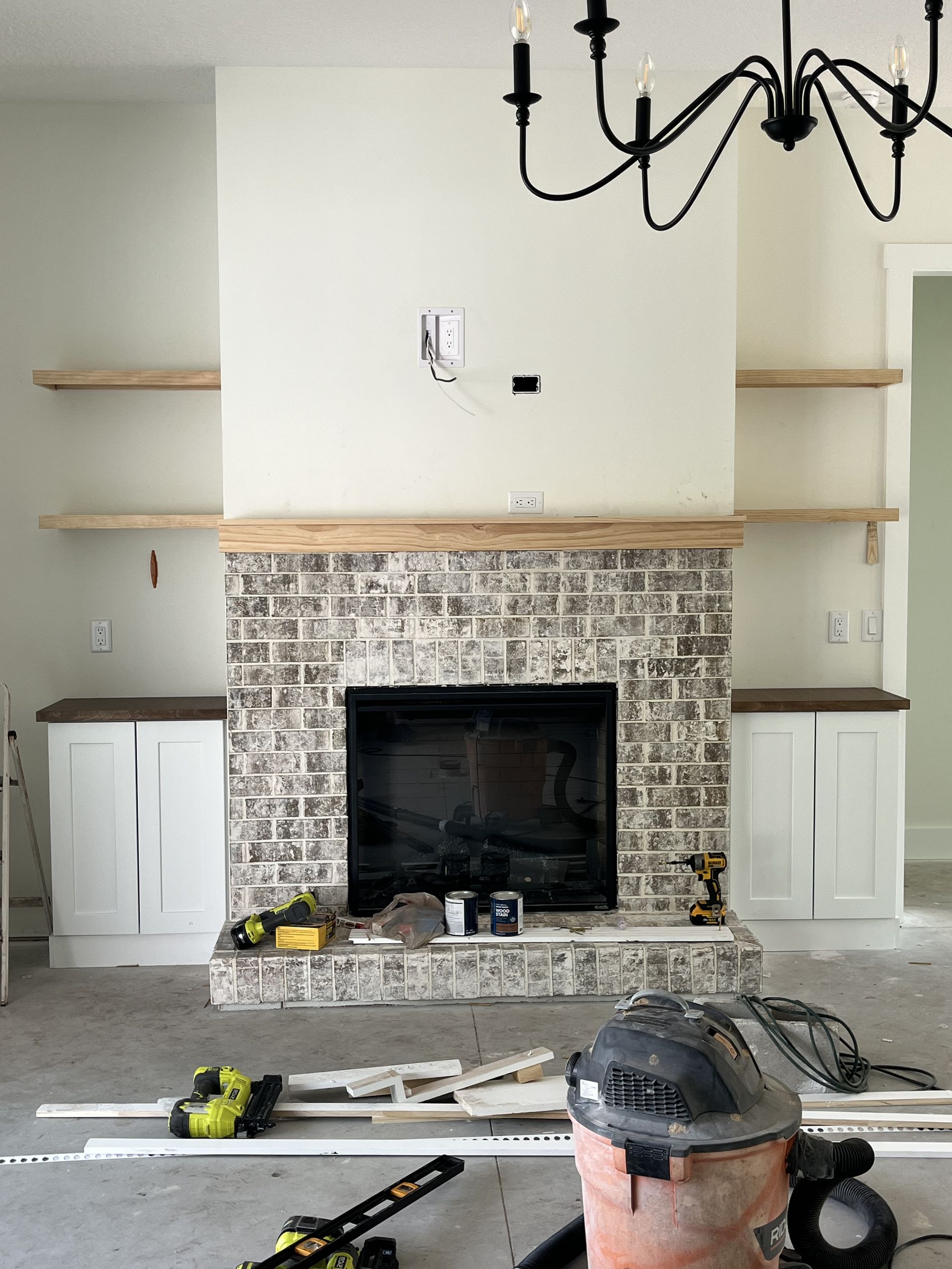 Living room with brick fireplace, built-in shelves, and a chandelier during renovation with tools on the floor