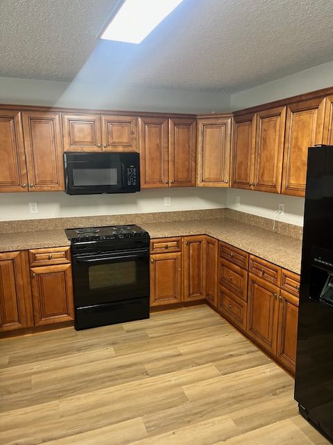Empty kitchen with wooden cabinets, black appliances, and light wood flooring.