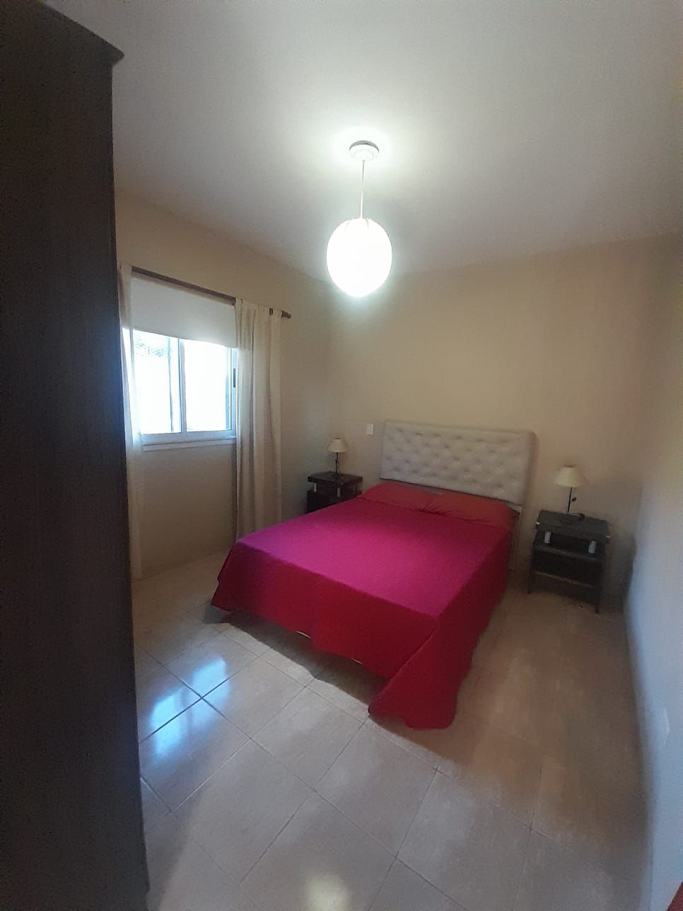 Habitación pequeña con sofá cama, mesa de comedor, refrigerador y techo con vigas de madera. Entra mucha luz natural.