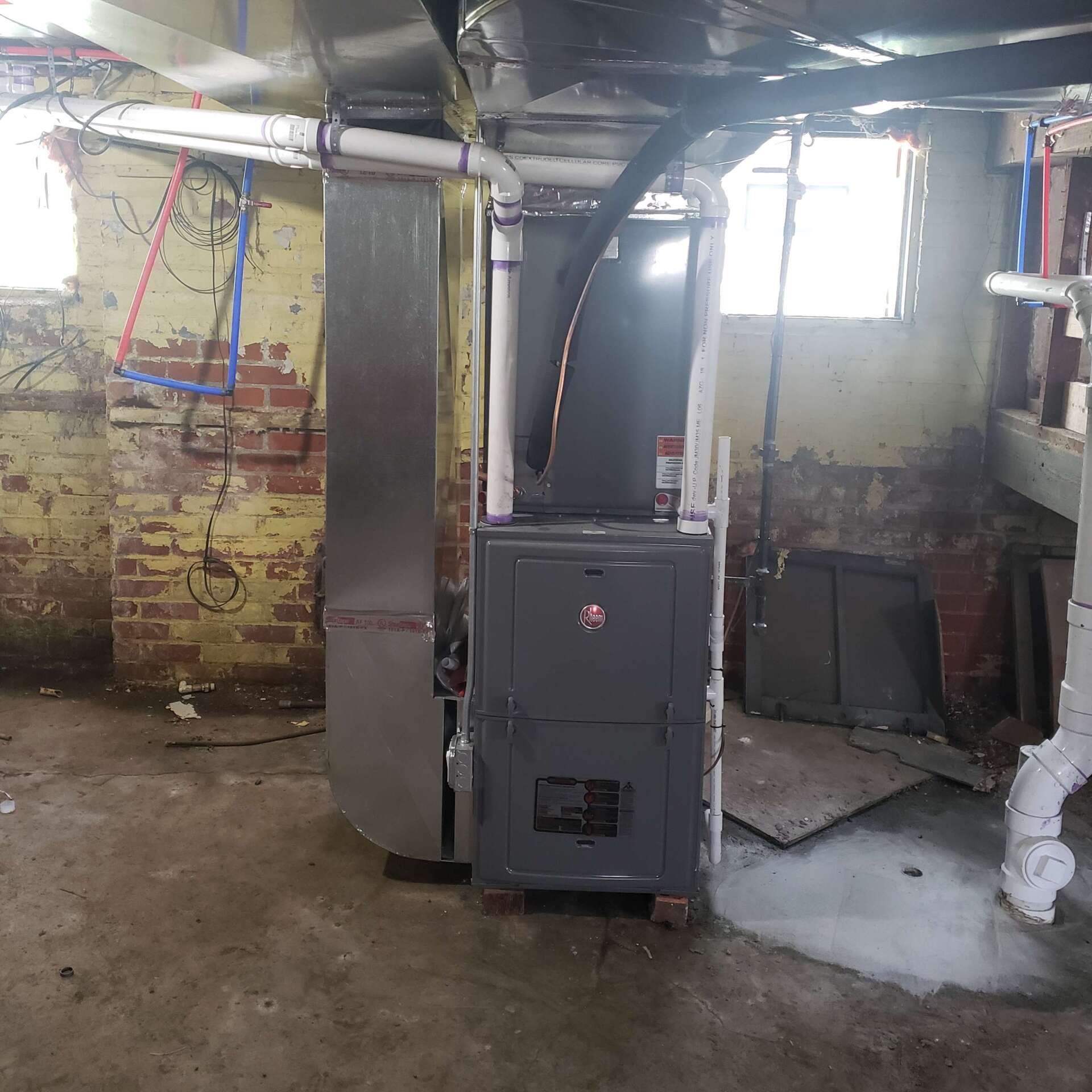 A furnace in a basement with ductwork and exposed brick walls.