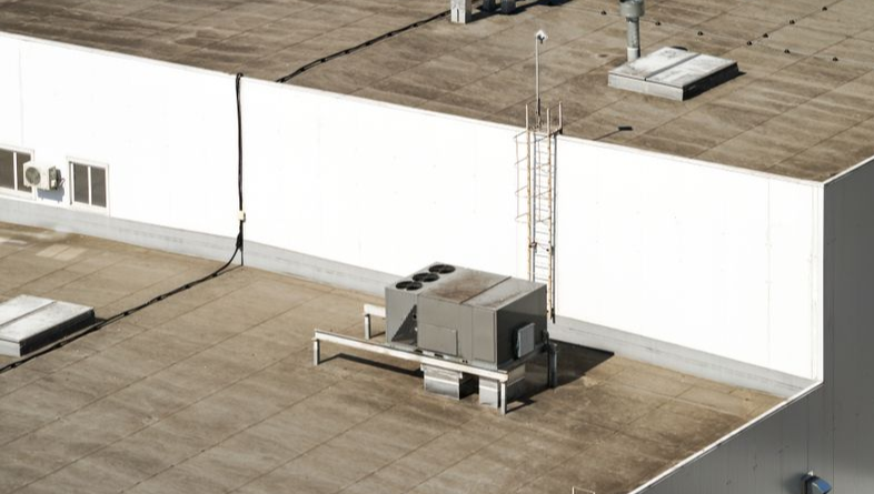 Man on ladder, working on HVAC ductwork in a room with beige and white walls.