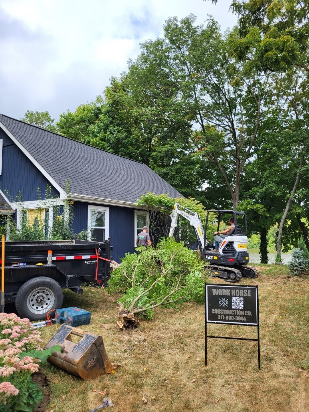 A man is driving an excavator in front of a blue house .