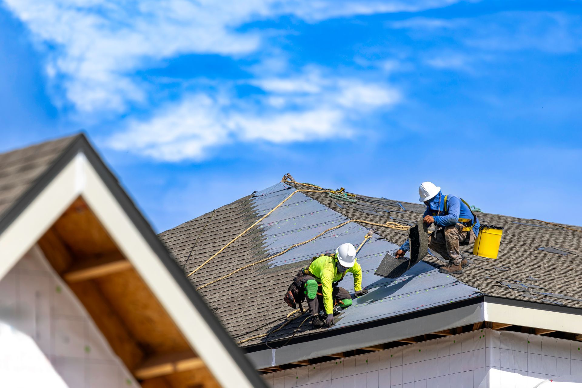 Roofing contractor crew installing new asphalt shingles on a residential roof. Roofing contractor crew installing new asphalt shingles on a residential roof.