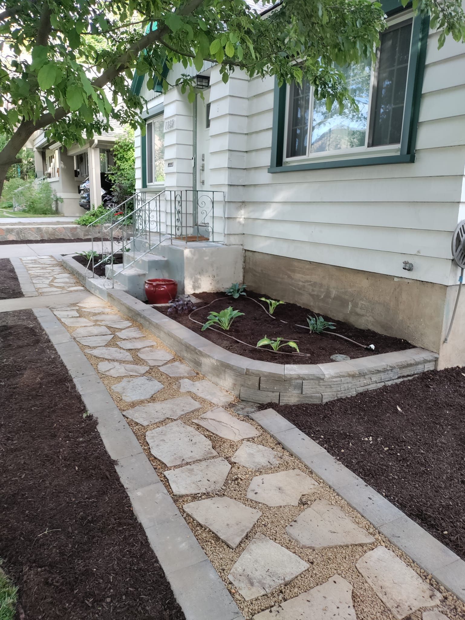 A stone walkway leading to a house with a garden in front of it.