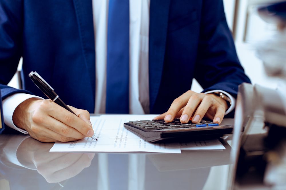 Person in Blue Suit Writing on Paper With Pen, Using a Calculator — Blue Chip Bookkeeping in Newcastle, NSW