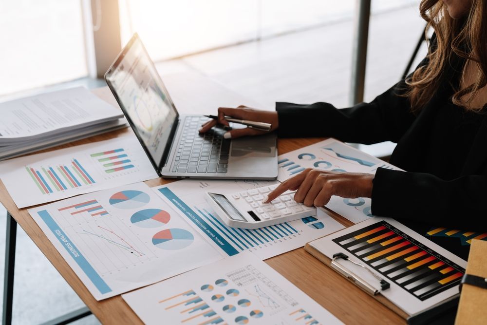 Person Using Laptop and Calculator at a Desk With Financial Charts and Documents — Blue Chip Bookkeeping in Newcastle, NSW