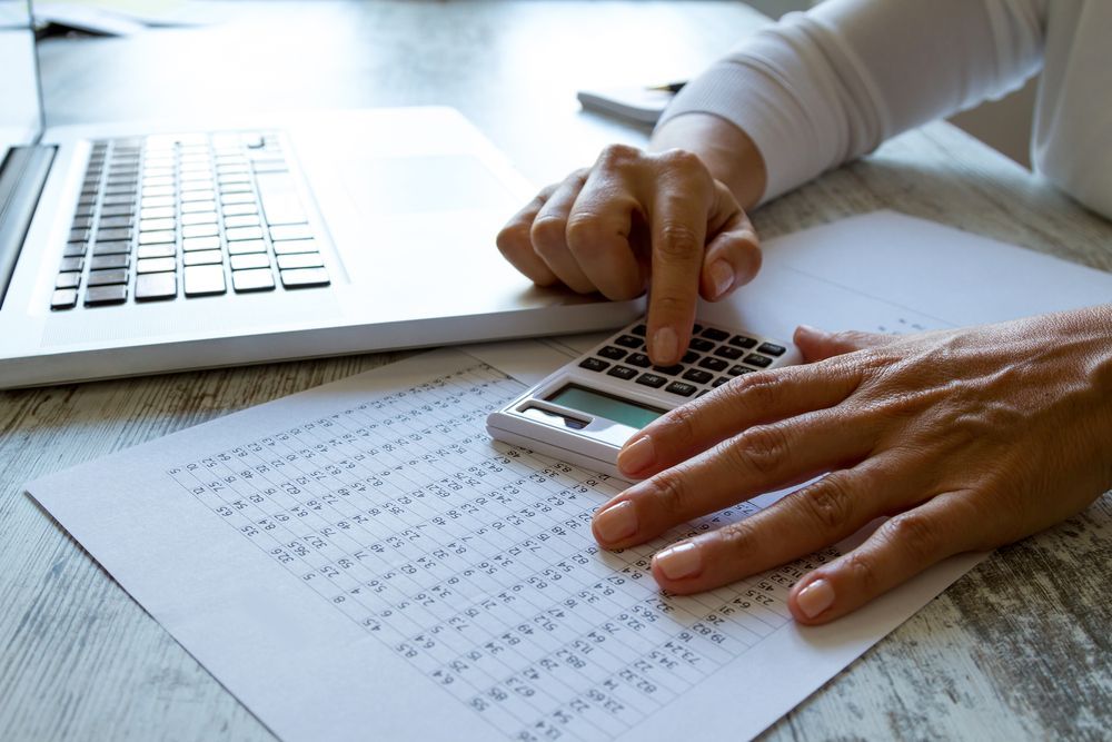 Person Using a Calculator While Working on a Laptop and Reviewing a Spreadsheet — Blue Chip Bookkeeping in Mackay, QLD