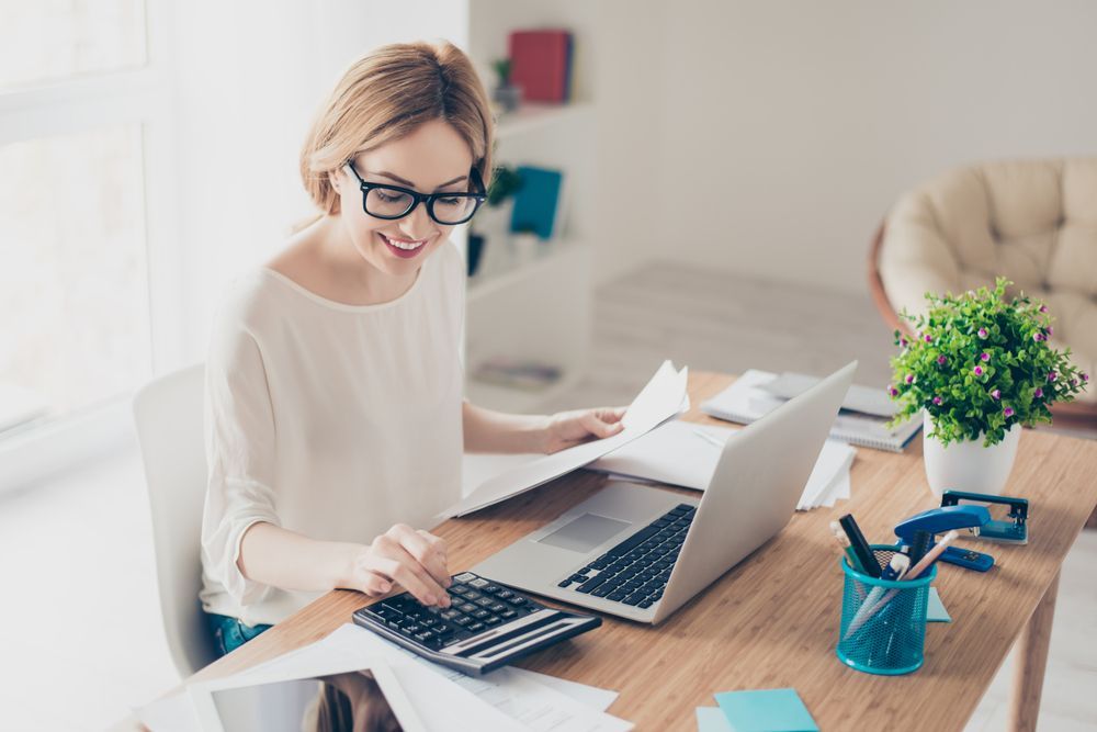 Woman Using a Calculator and Laptop at a Desk With Papers — Blue Chip Bookkeeping in Newcastle, NSW