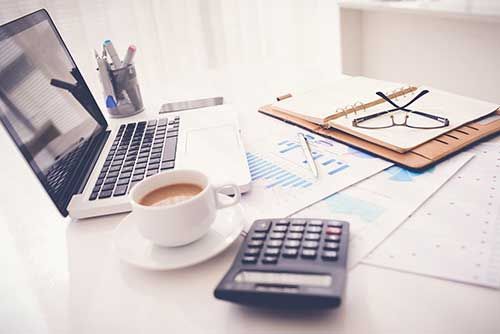 A Desk with A Laptop, Calculator, Cup Of Coffee And Glasses — Blue Chip Bookkeeping In Nome, QLD