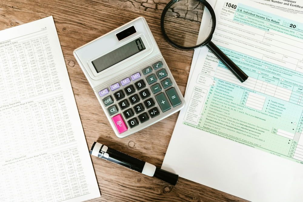 A Calculator, Magnifying Glass, Pen, And Tax Forms Are On A Wooden Table — Blue Chip Bookkeeping In Townsville, QLD