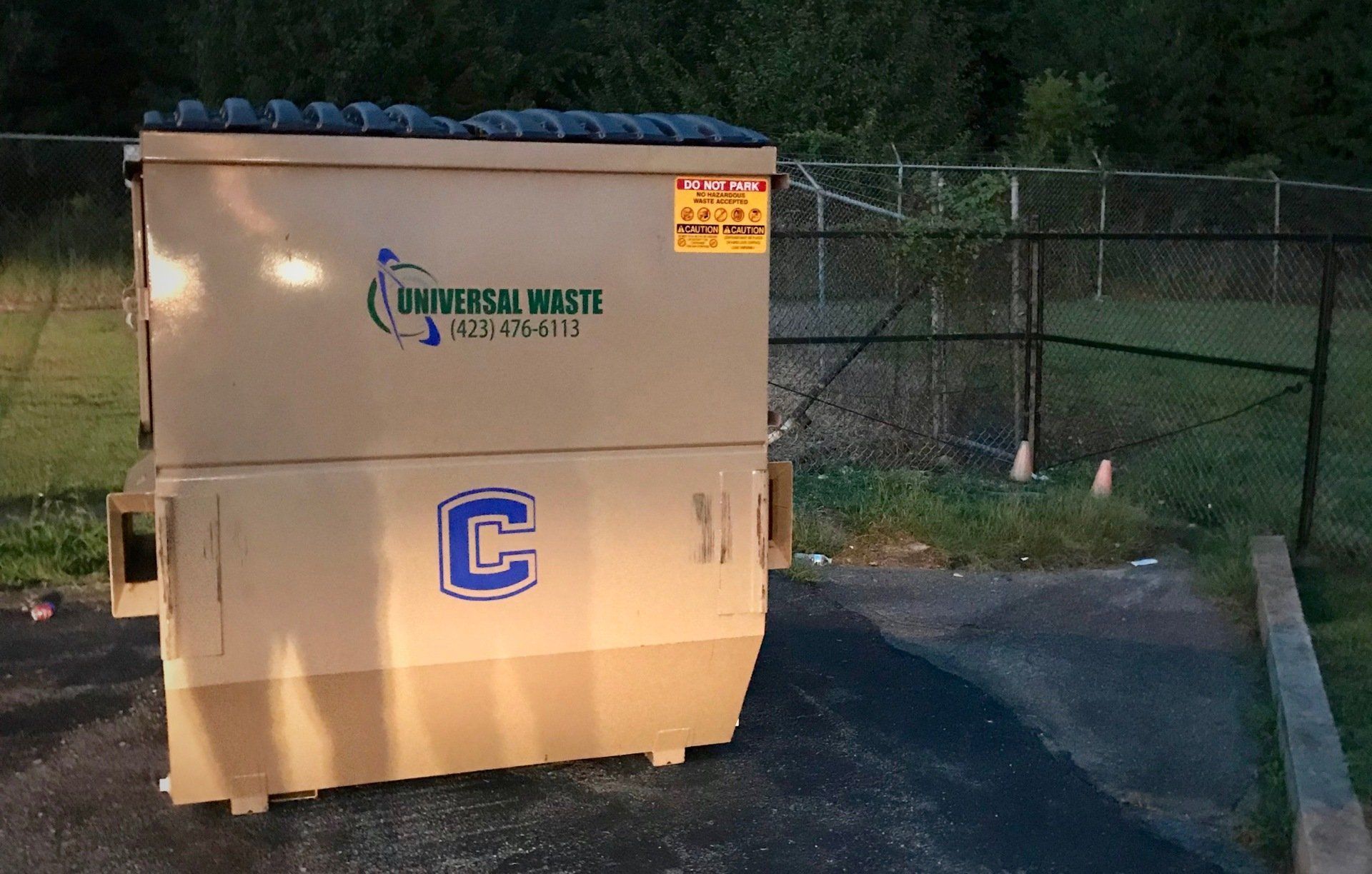 A dumpster with the letter c on it is parked in front of a fence.