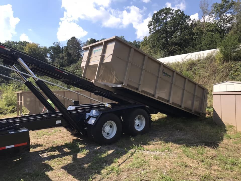 A dumpster is sitting on top of a trailer in a field.