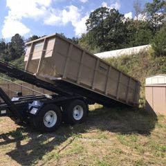 A dumpster on a trailer with a shed in the background