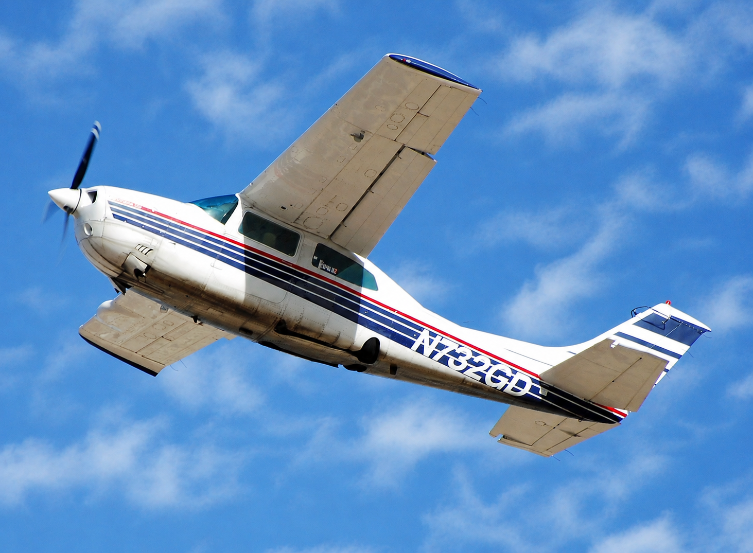 Small white propeller Cessna 210 airplane with red and blue stripes flying against a blue sky