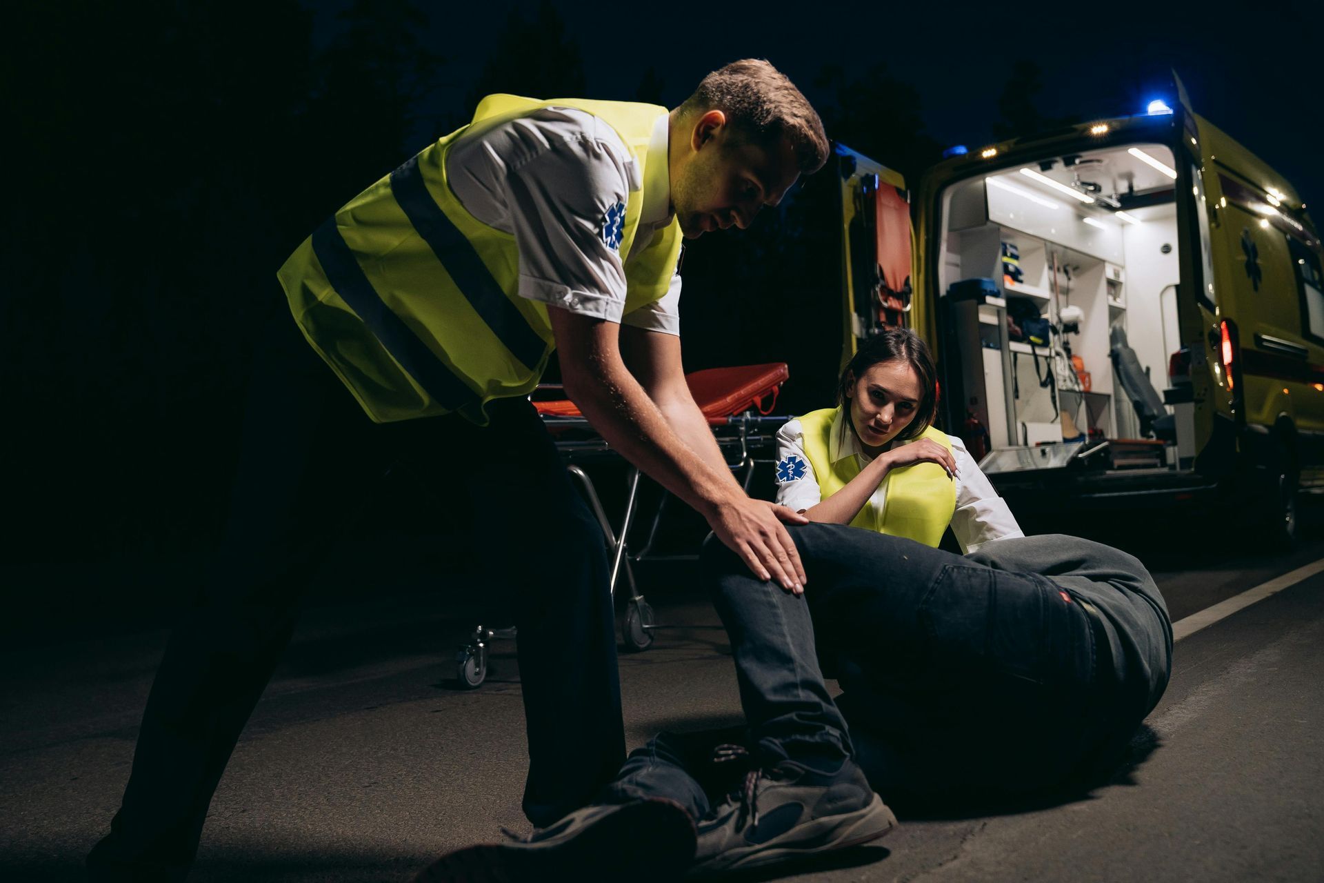 Paramedics loading an injured person onto a stretcher beside an ambulance at night