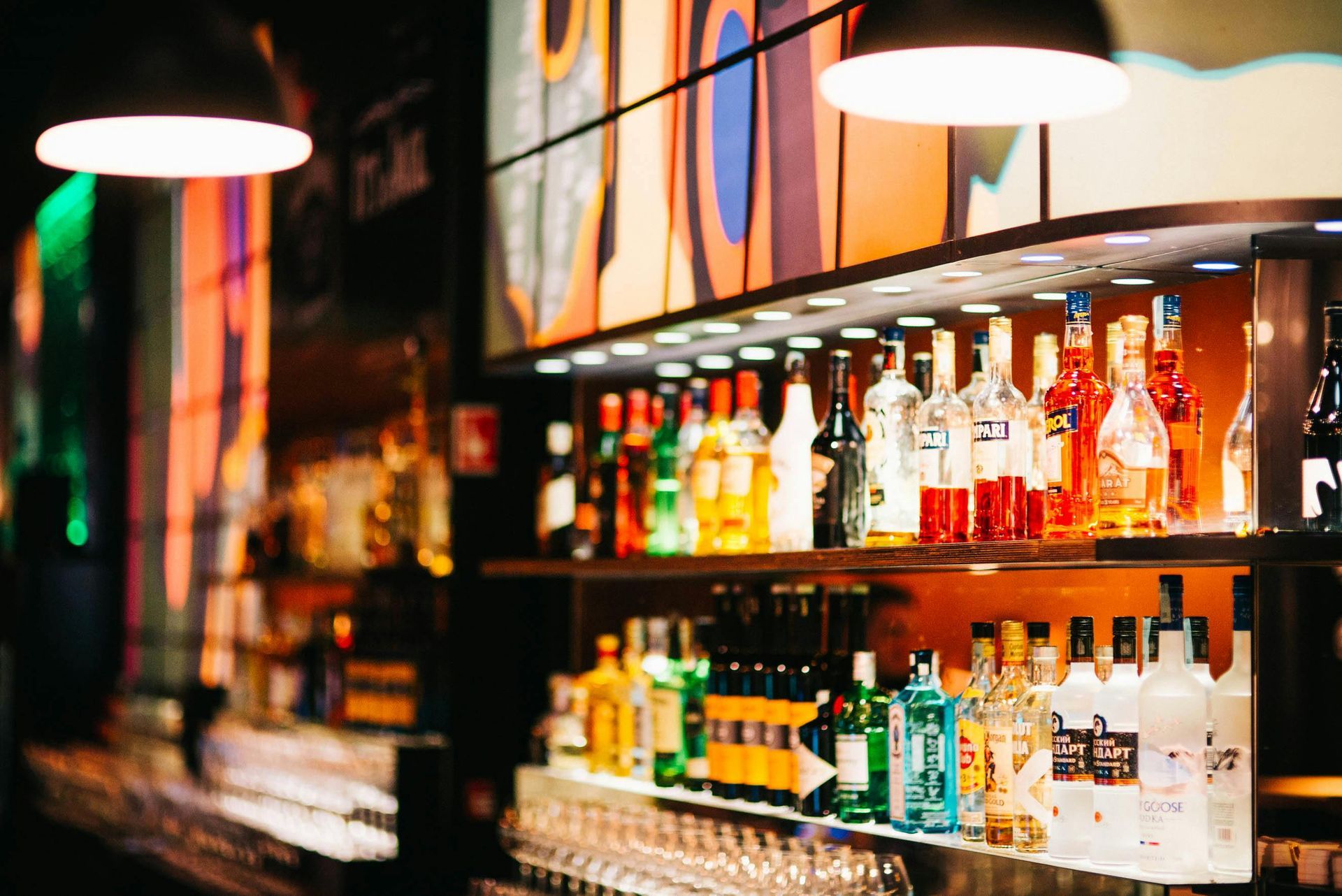 Bar shelves lined with colorful liquor bottles under warm pendant lights in a dimly lit bar