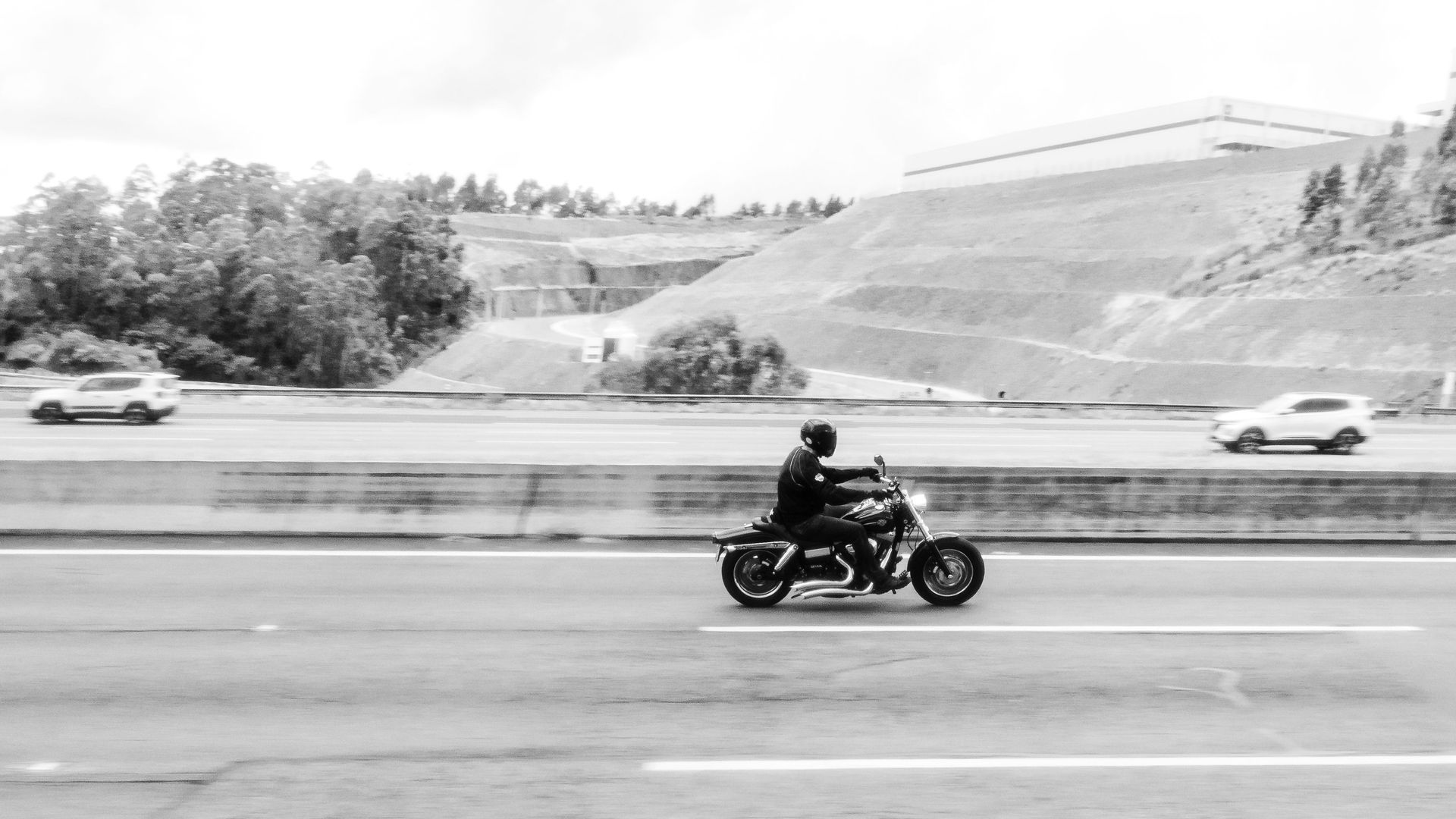 Motorcyclist riding on a highway with cars and grassy hills in the background