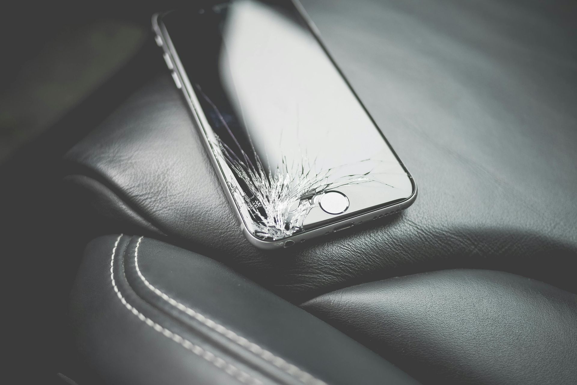Cracked smartphone lying on a black leather car seat close-up
