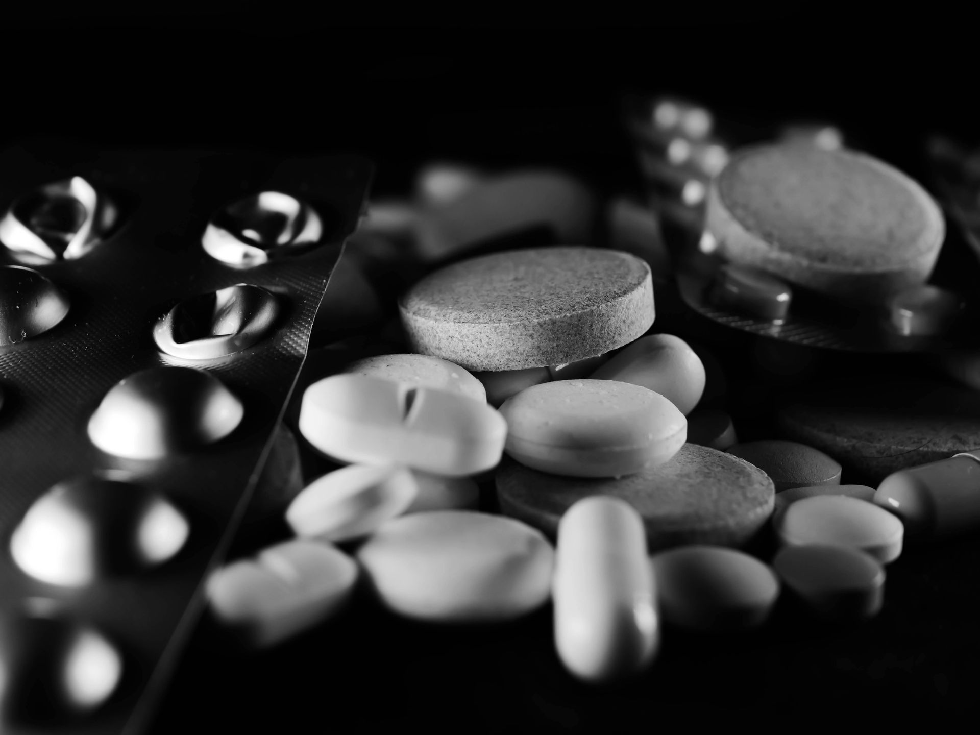 Assorted pills and tablets on a dark surface, arranged in blister packs and loose piles