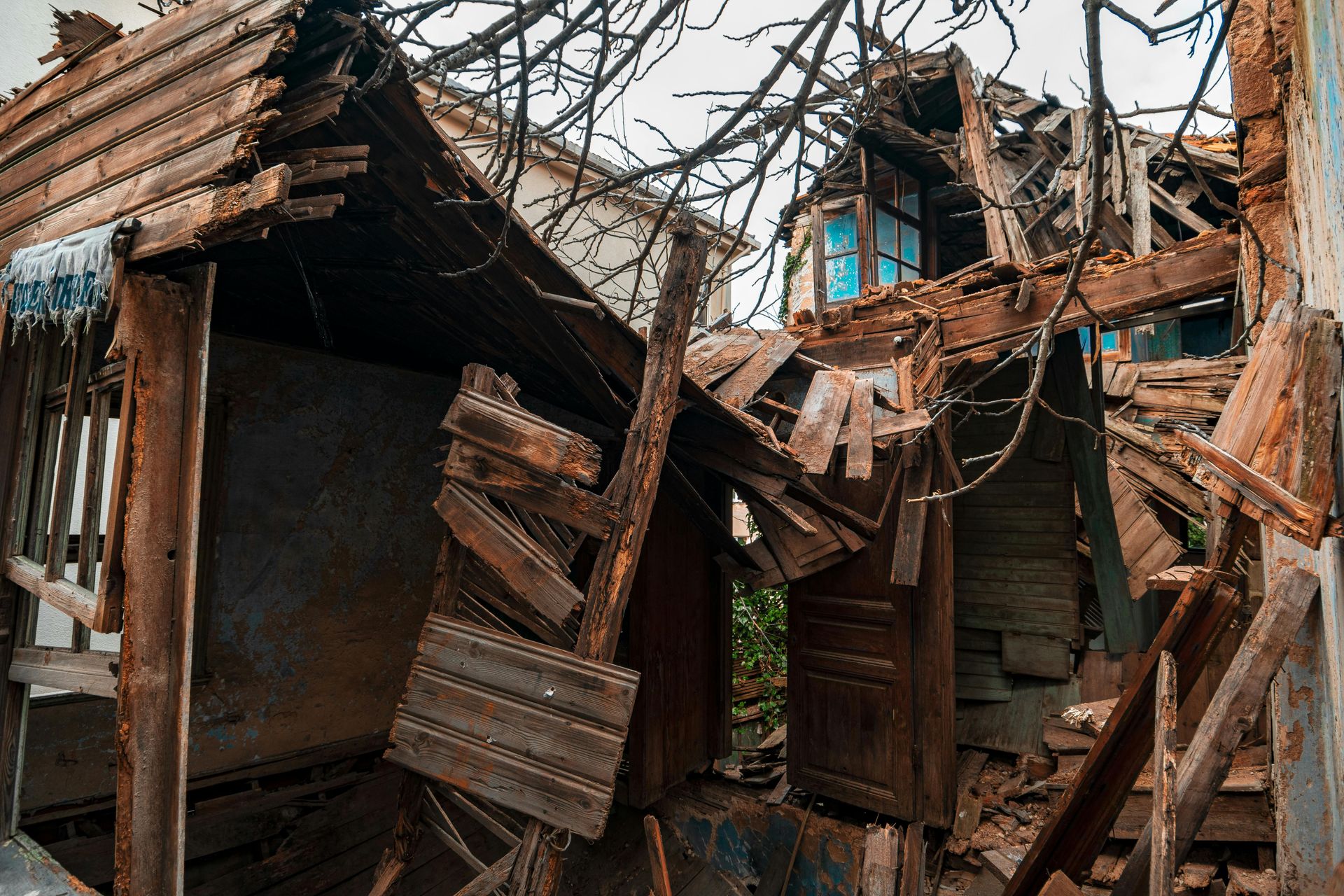 Collapsed wooden house with broken walls and roof, debris scattered among bare tree branches